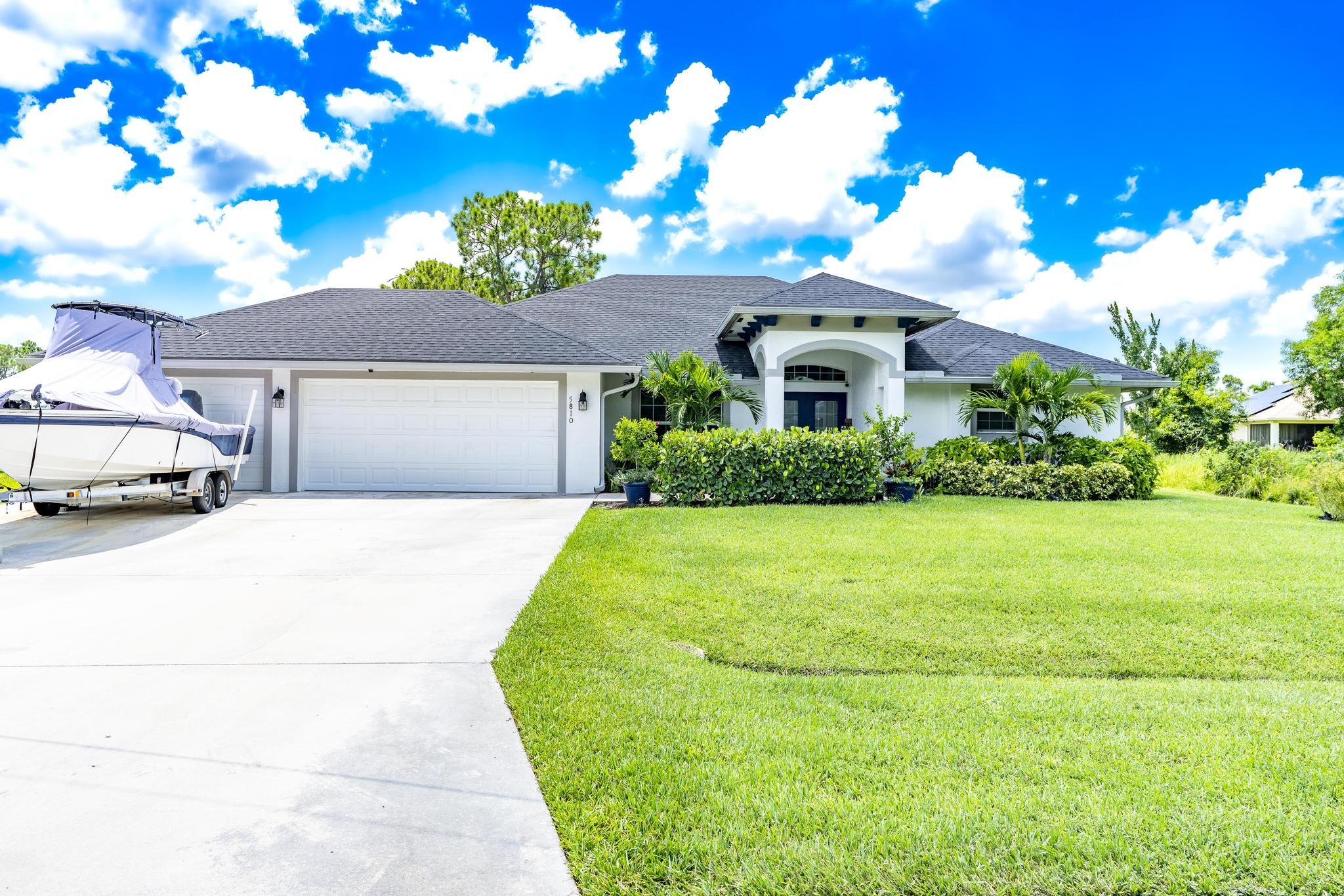 White single-story home with an arched entry, two-car garage, and covered boat in the driveway.