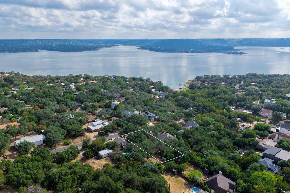 A wooded residential lot outlined among trees and homes beside a broad lake.