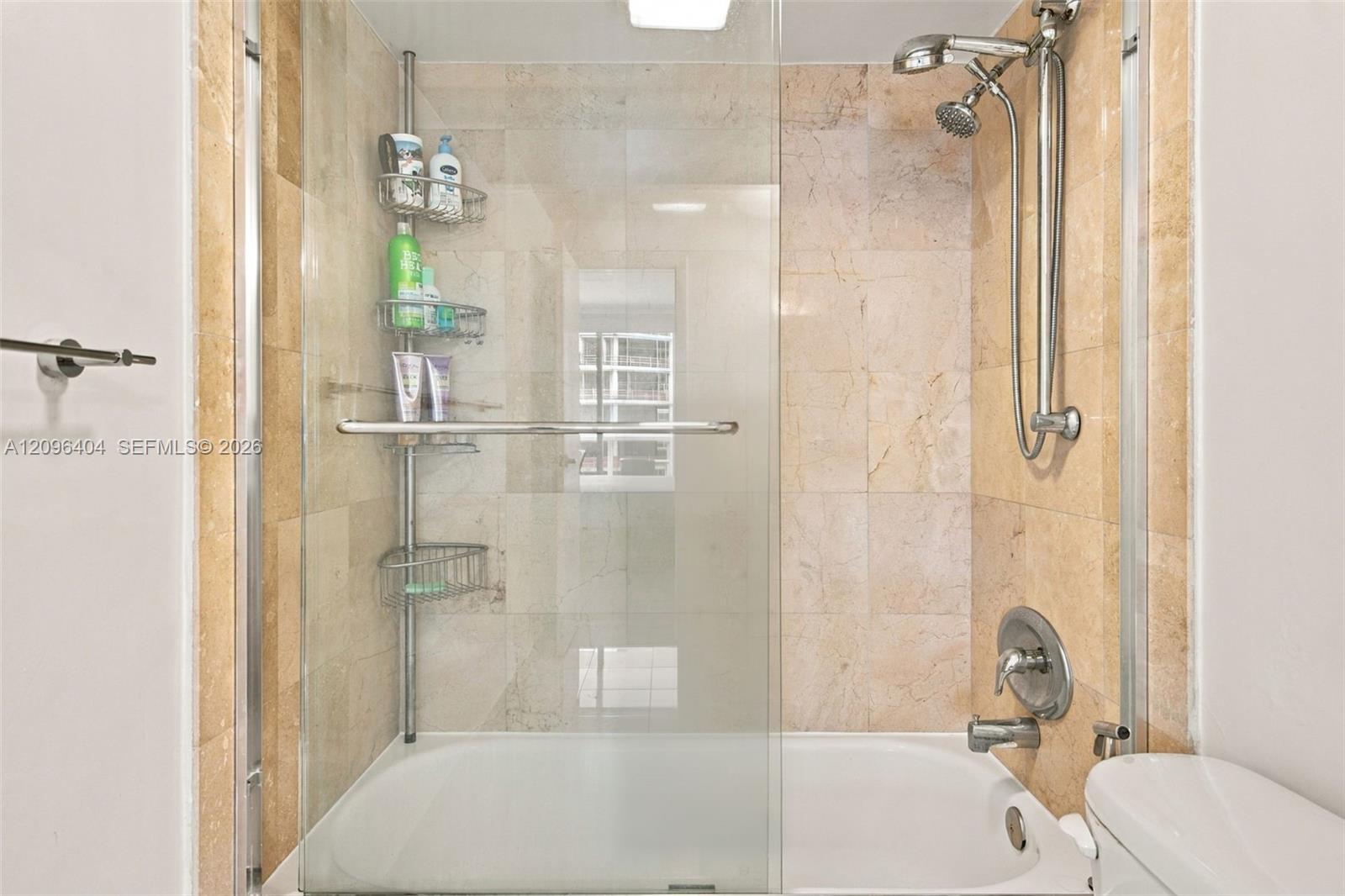 Bathroom with a glass-enclosed bathtub and beige marble tile.