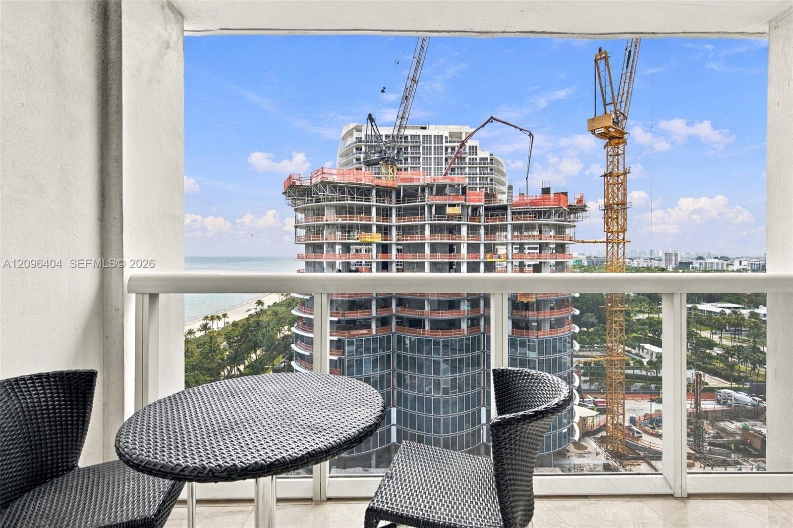 Condo balcony with woven furniture overlooking a high-rise under construction and the ocean.
