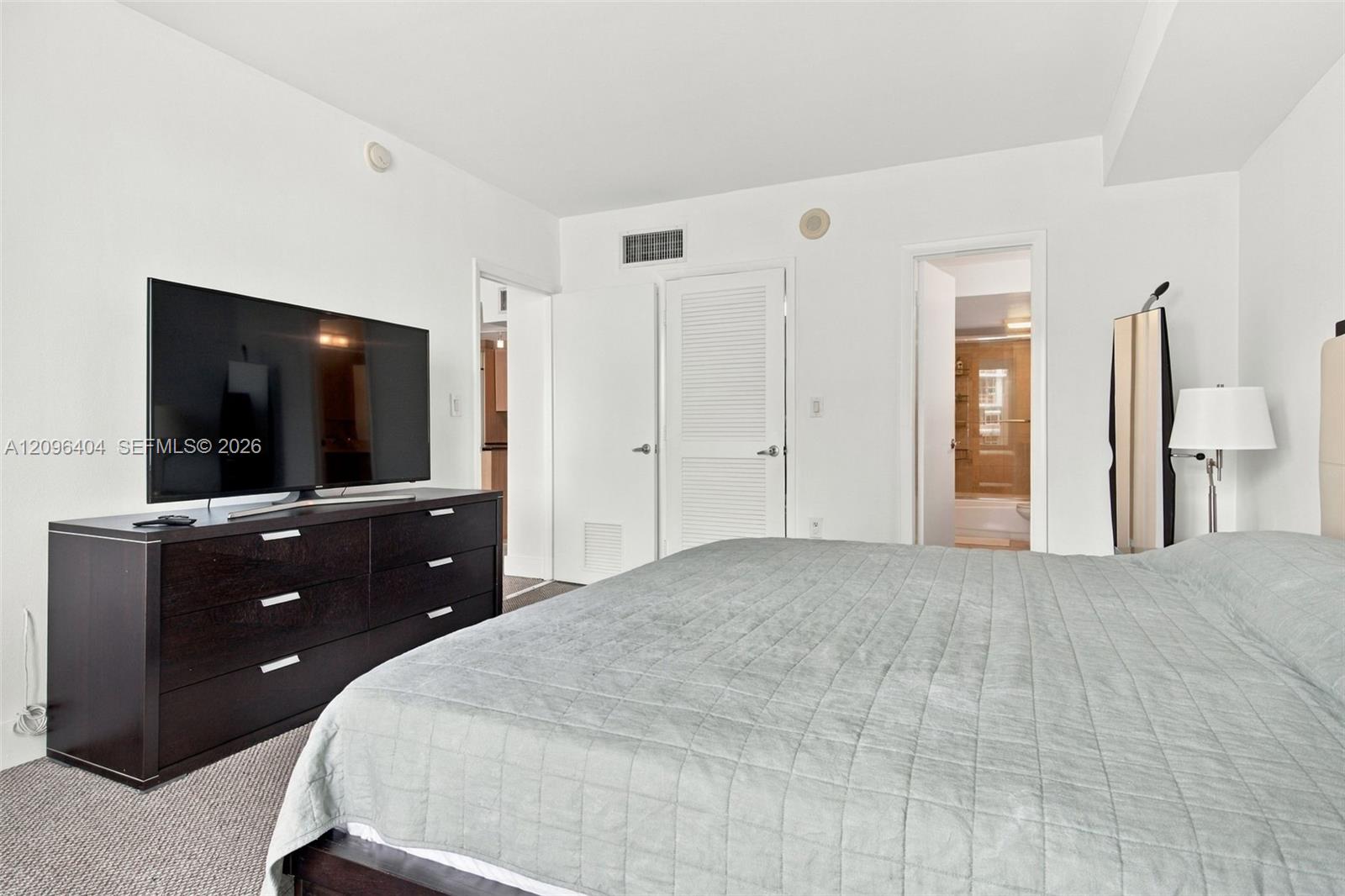 Furnished bedroom with a large gray-quilted bed and a television on a dark dresser.