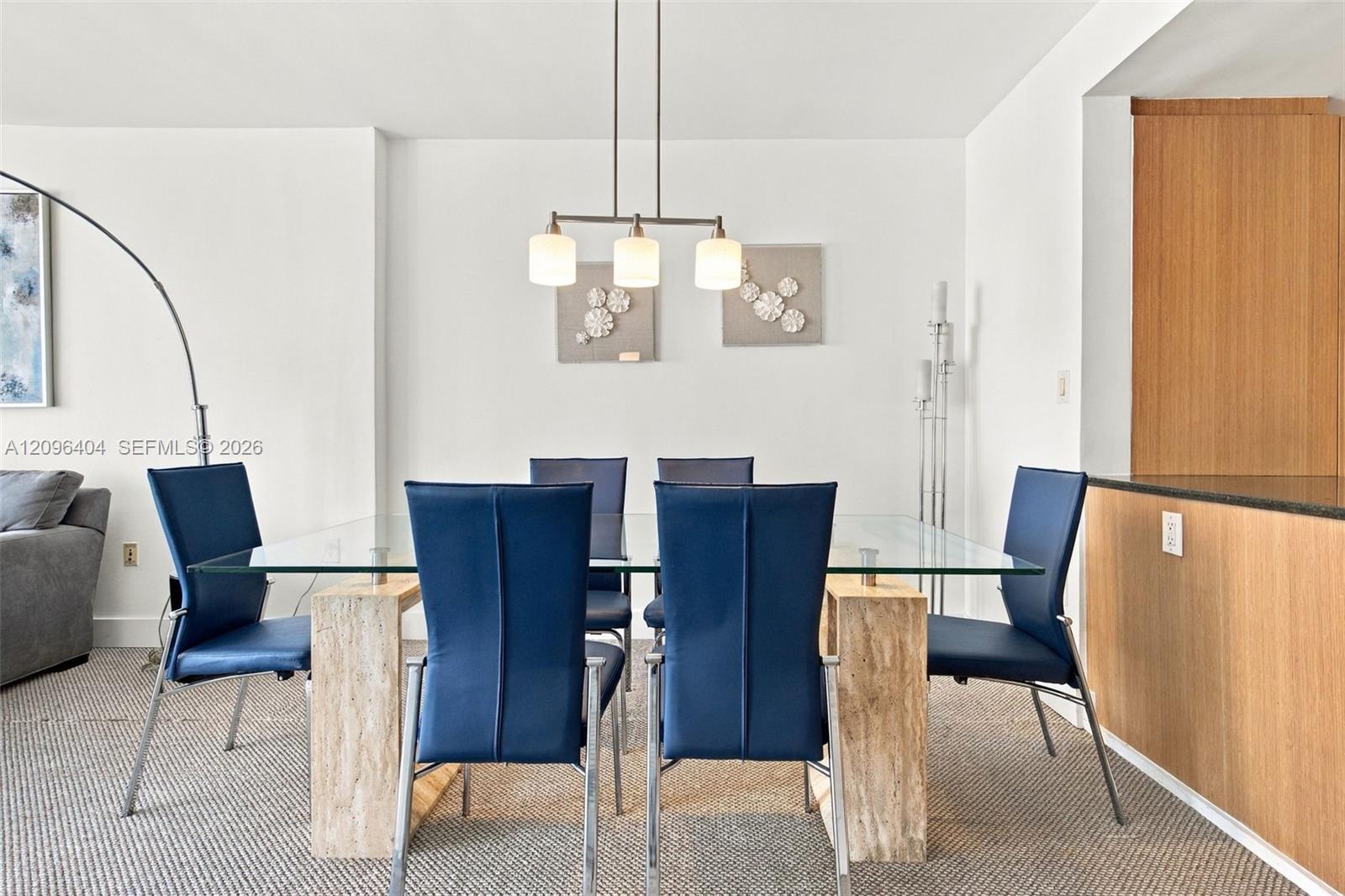 Dining area with a glass table, navy chairs, and a wood-paneled kitchen counter.