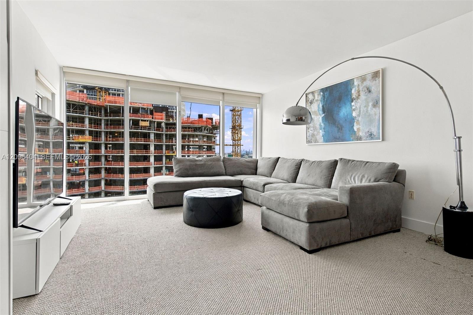 High-rise living room with a gray sectional and corner windows overlooking a building under construction.