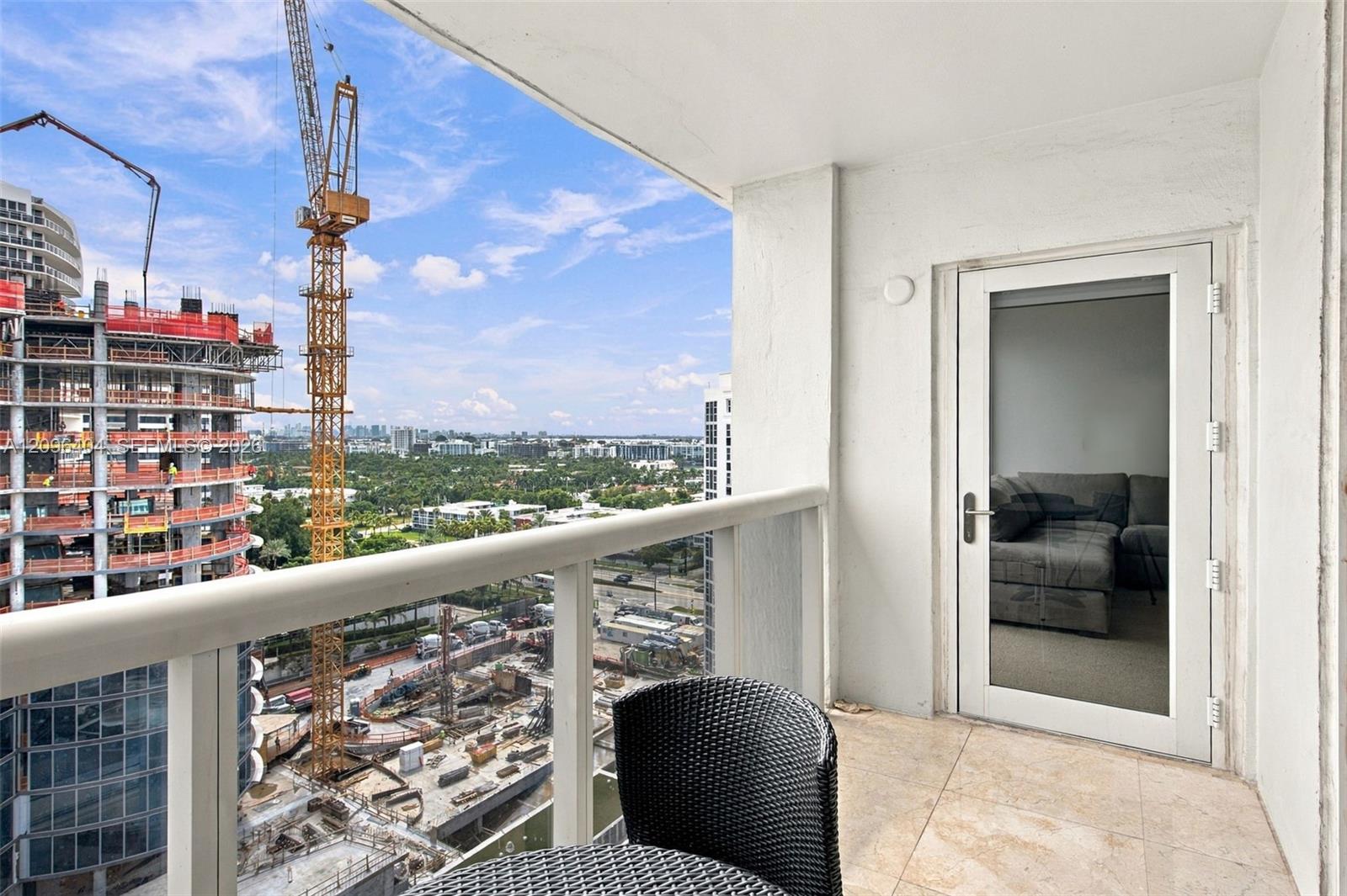 Condo balcony with wicker seating overlooking construction cranes, greenery, and a distant city skyline.