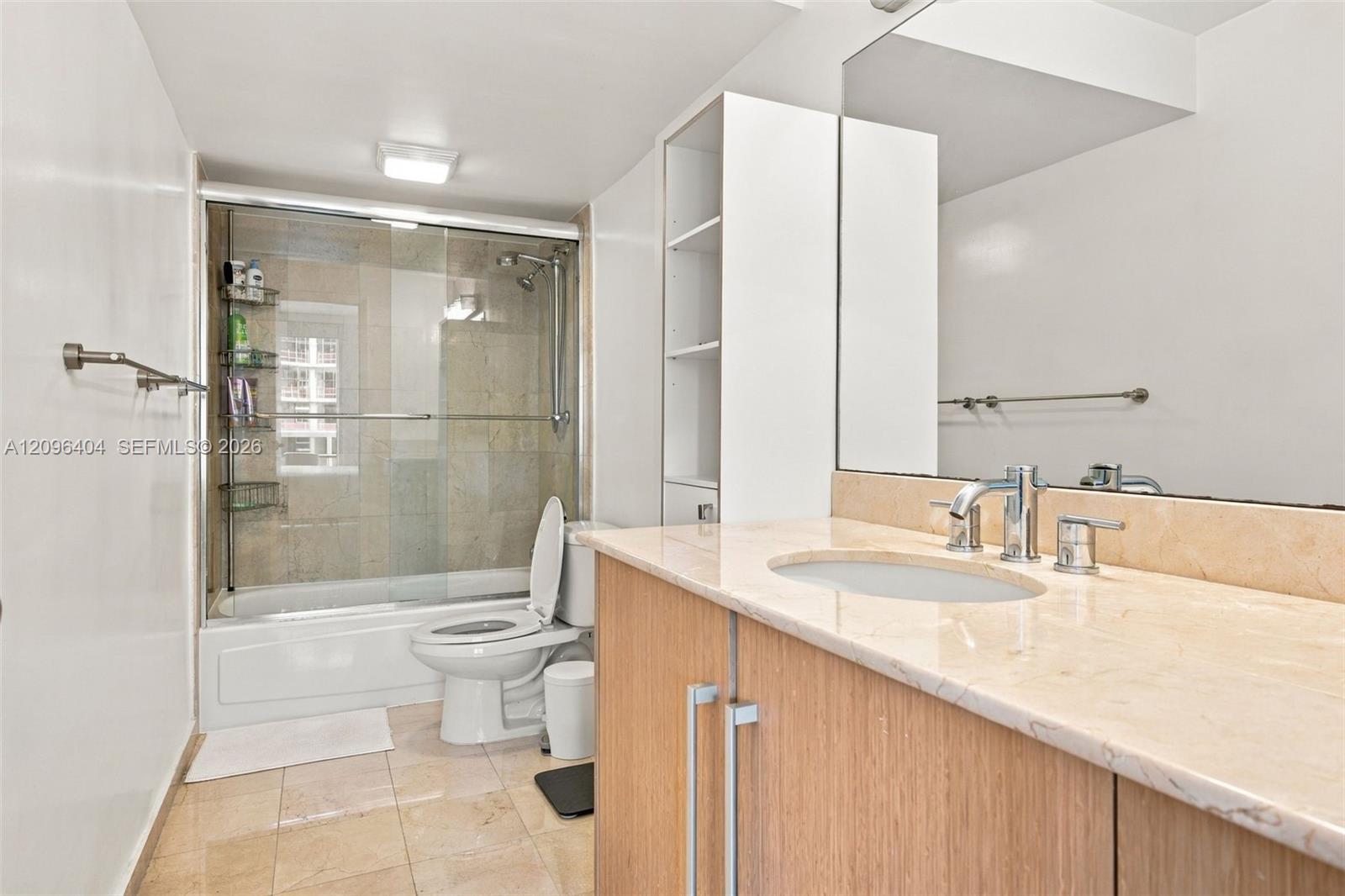 Bathroom with glass-enclosed tub and shower, wood vanity, stone counter, and large mirror.