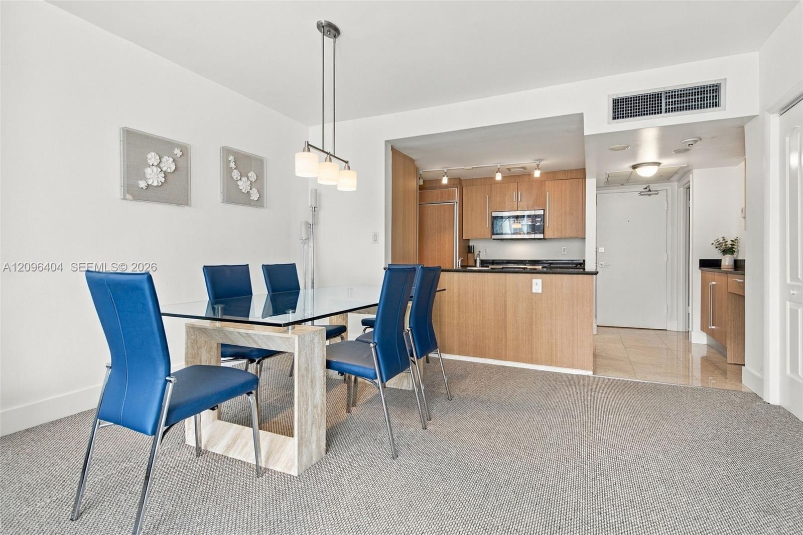Dining area with blue chairs and a glass-top table beside a wood-cabinet kitchen.