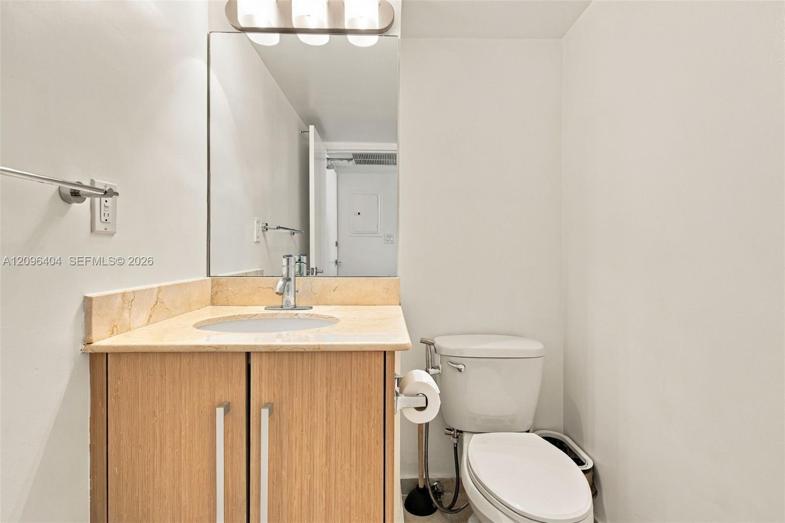 Bathroom with a wood vanity, pale stone countertop, oval sink, and white toilet.