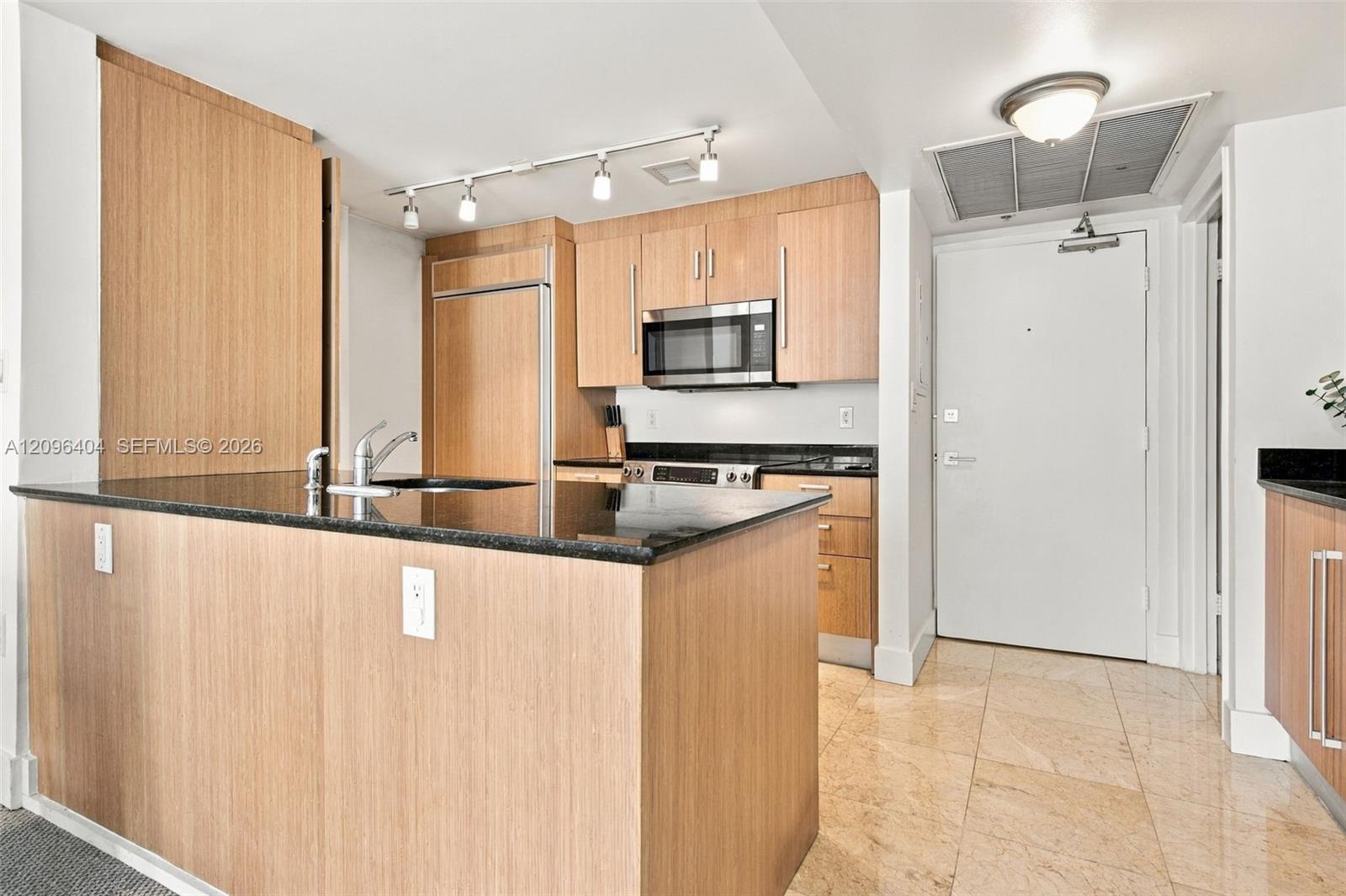 Condominium kitchen with a wood-paneled island, black countertops, and stainless steel appliances.