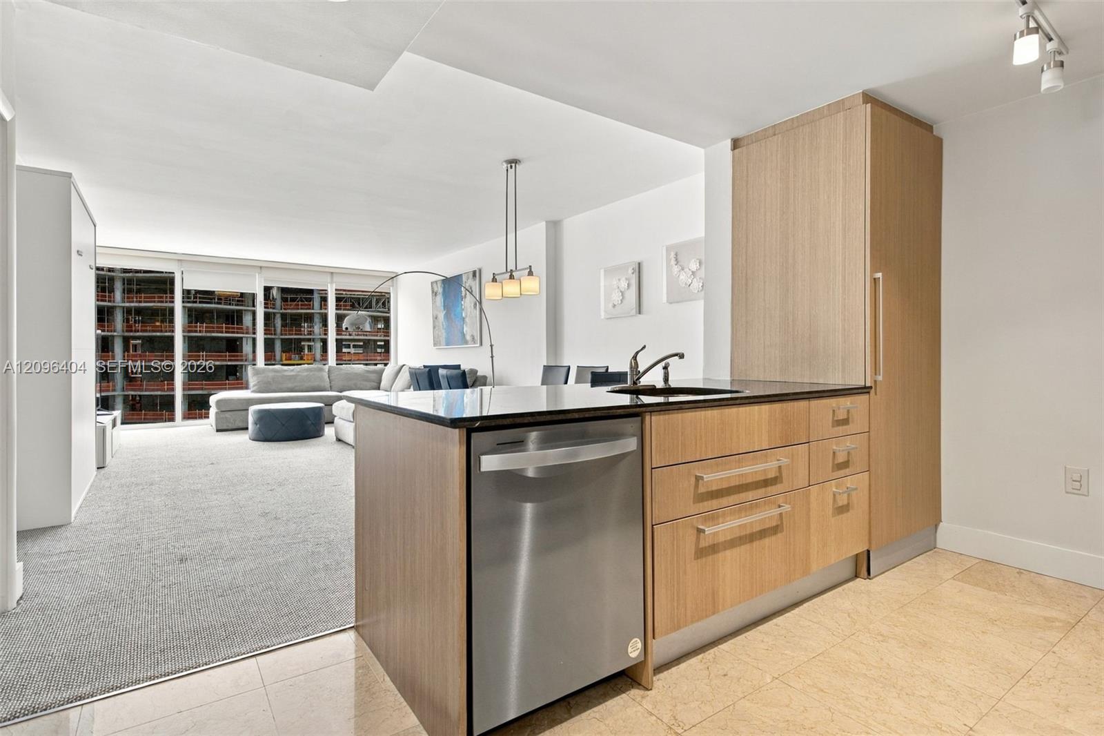 Open-plan condo kitchen with light wood cabinetry and a living area beside floor-to-ceiling windows.