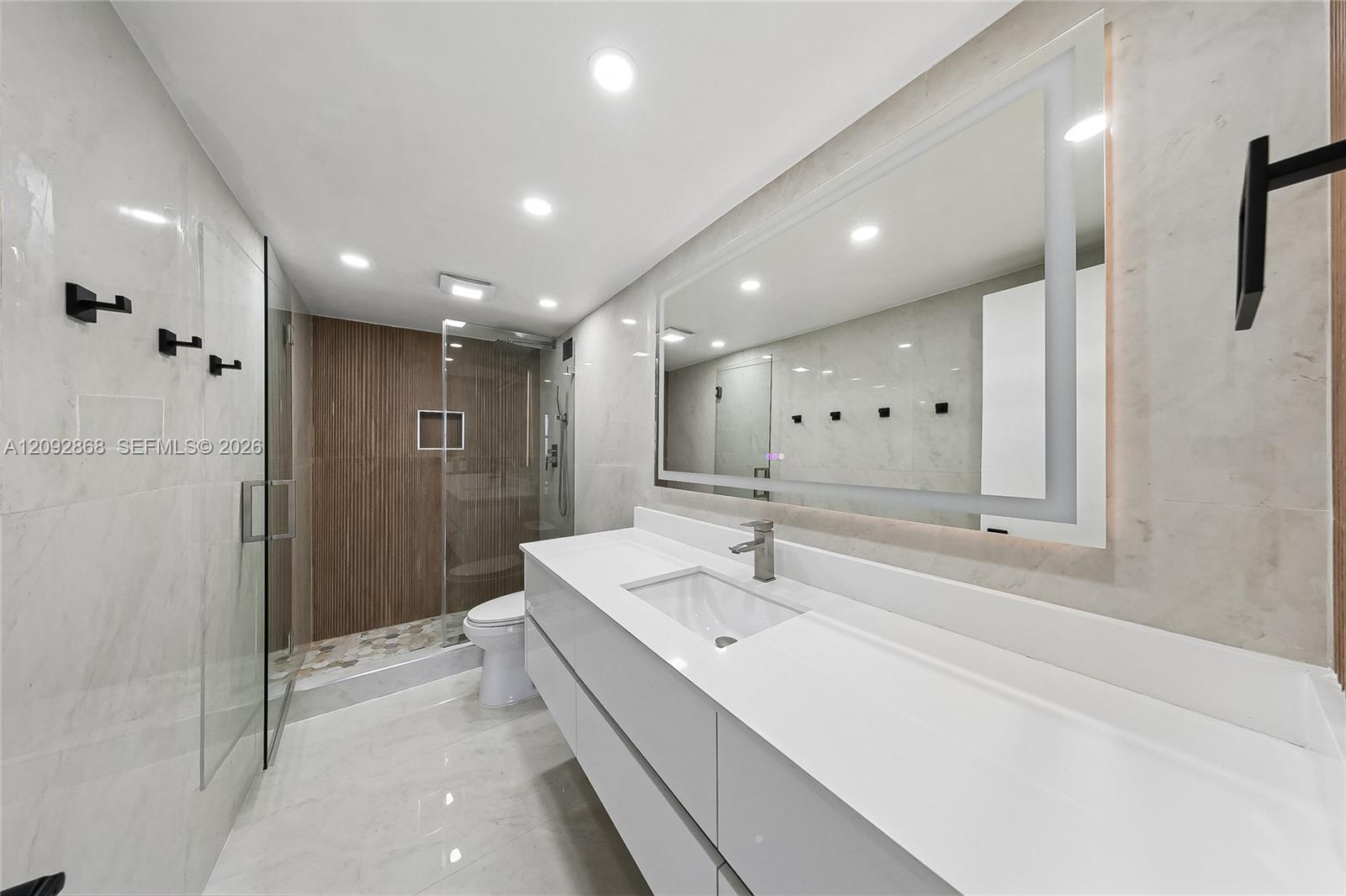 Modern marble-tiled bathroom with a long white vanity and glass shower featuring a wood-slat accent wall.