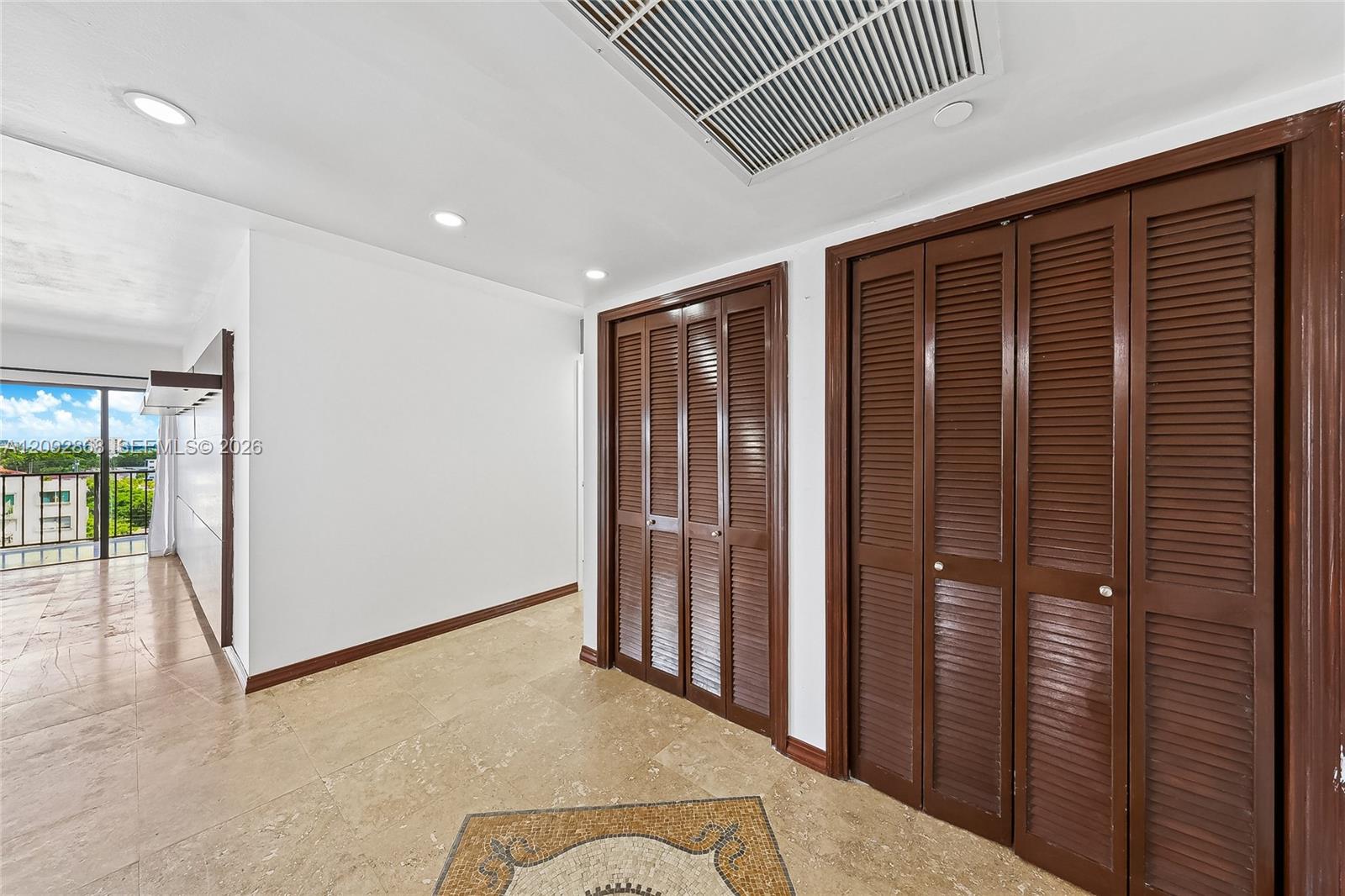 Condo hallway with dark wood louvered closet doors and beige tile flooring.