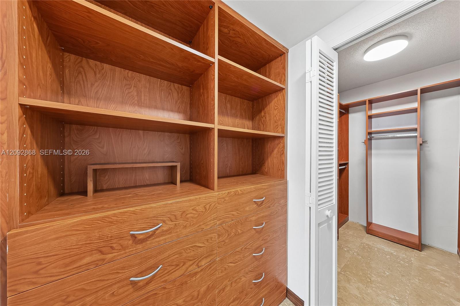 Walk-in closet with reddish wood built-in shelving and drawers beside hanging space.