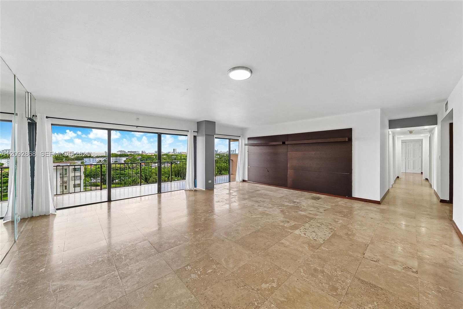 Vacant condo living area with stone tile floors, a dark wood feature wall, and balcony doors overlooking the city.