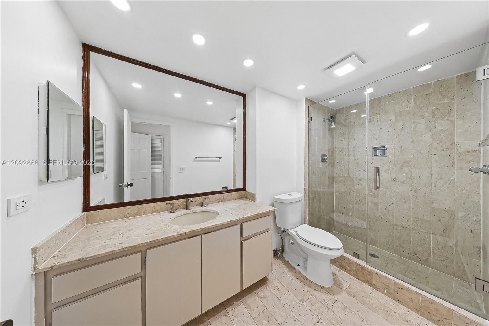Bathroom with a long stone vanity, large framed mirror, and glass-enclosed stone-tile shower.