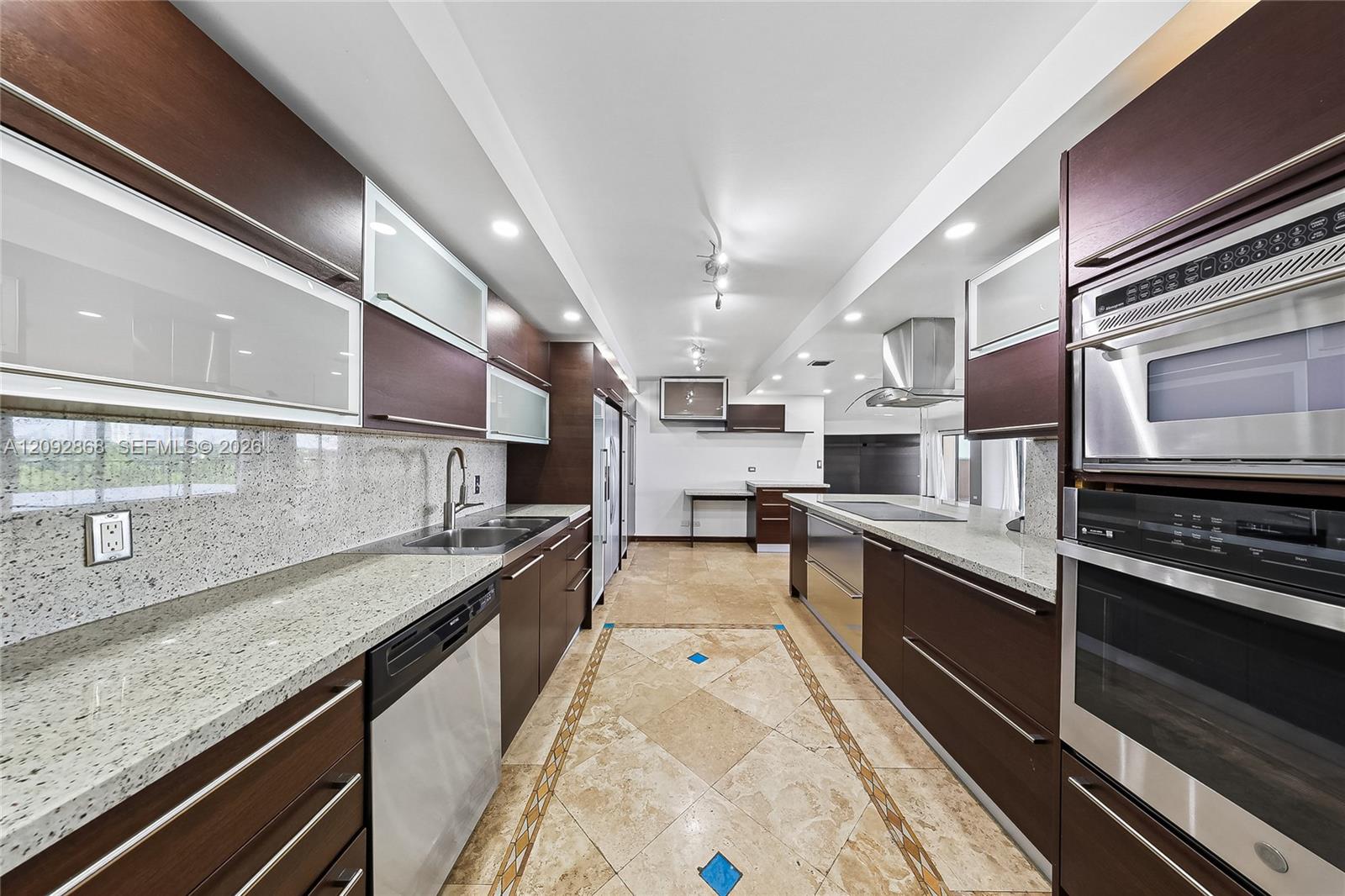Modern galley kitchen with dark wood cabinets, stone counters, and stainless steel appliances.