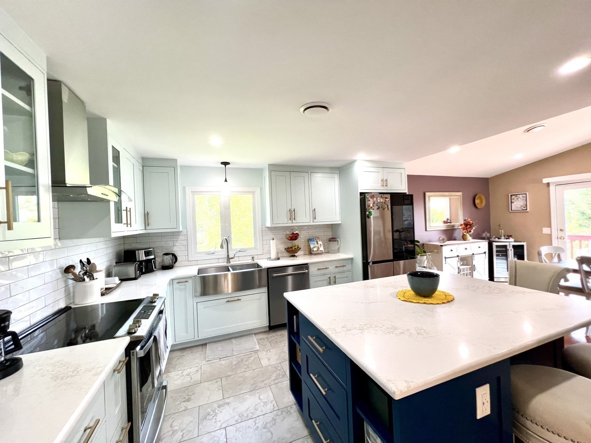 Bright kitchen with a large navy island, pale cabinets, and stainless steel appliances.