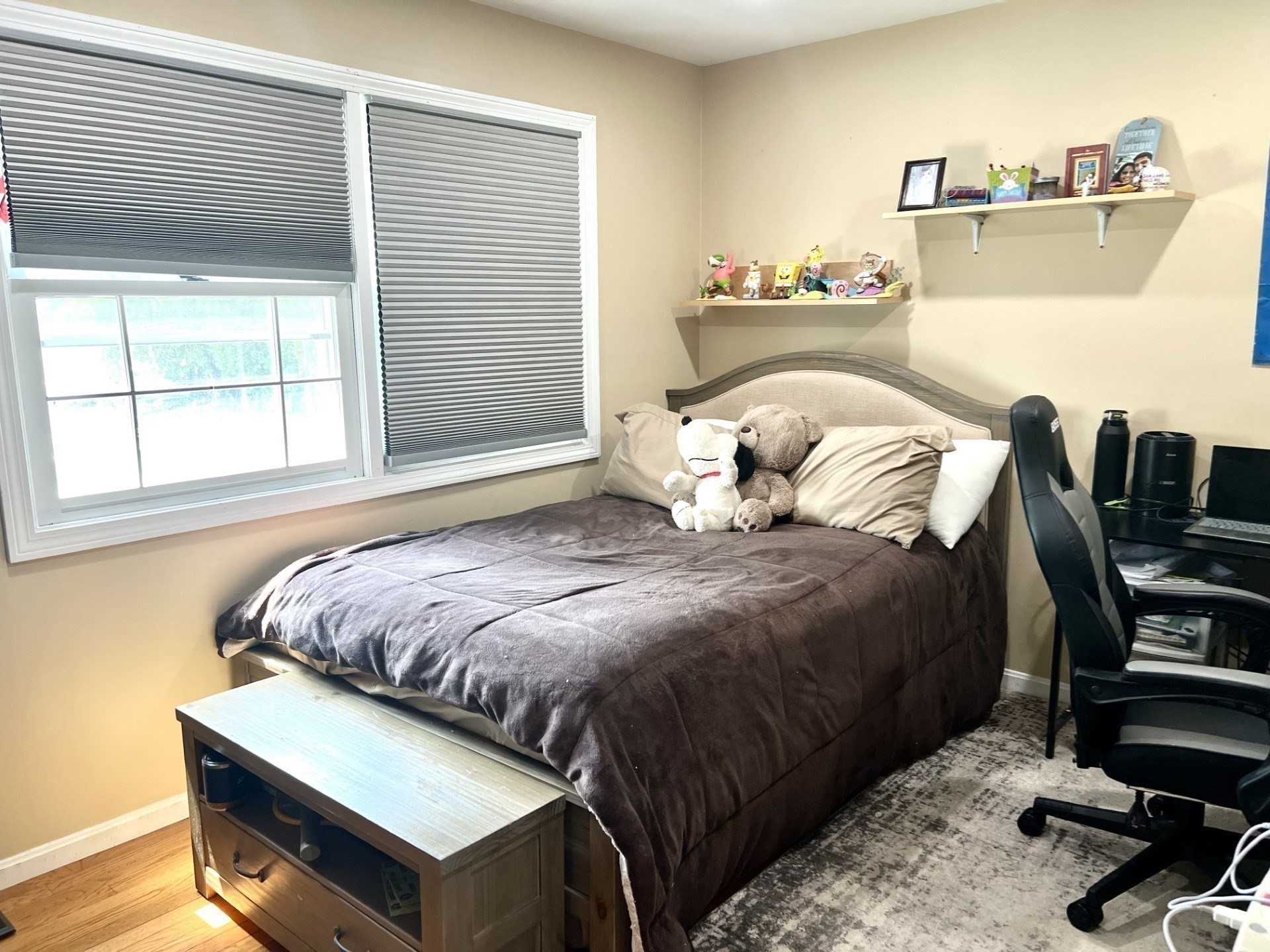 Bedroom with a large bed, stuffed animals, window blinds, and a desk chair.
