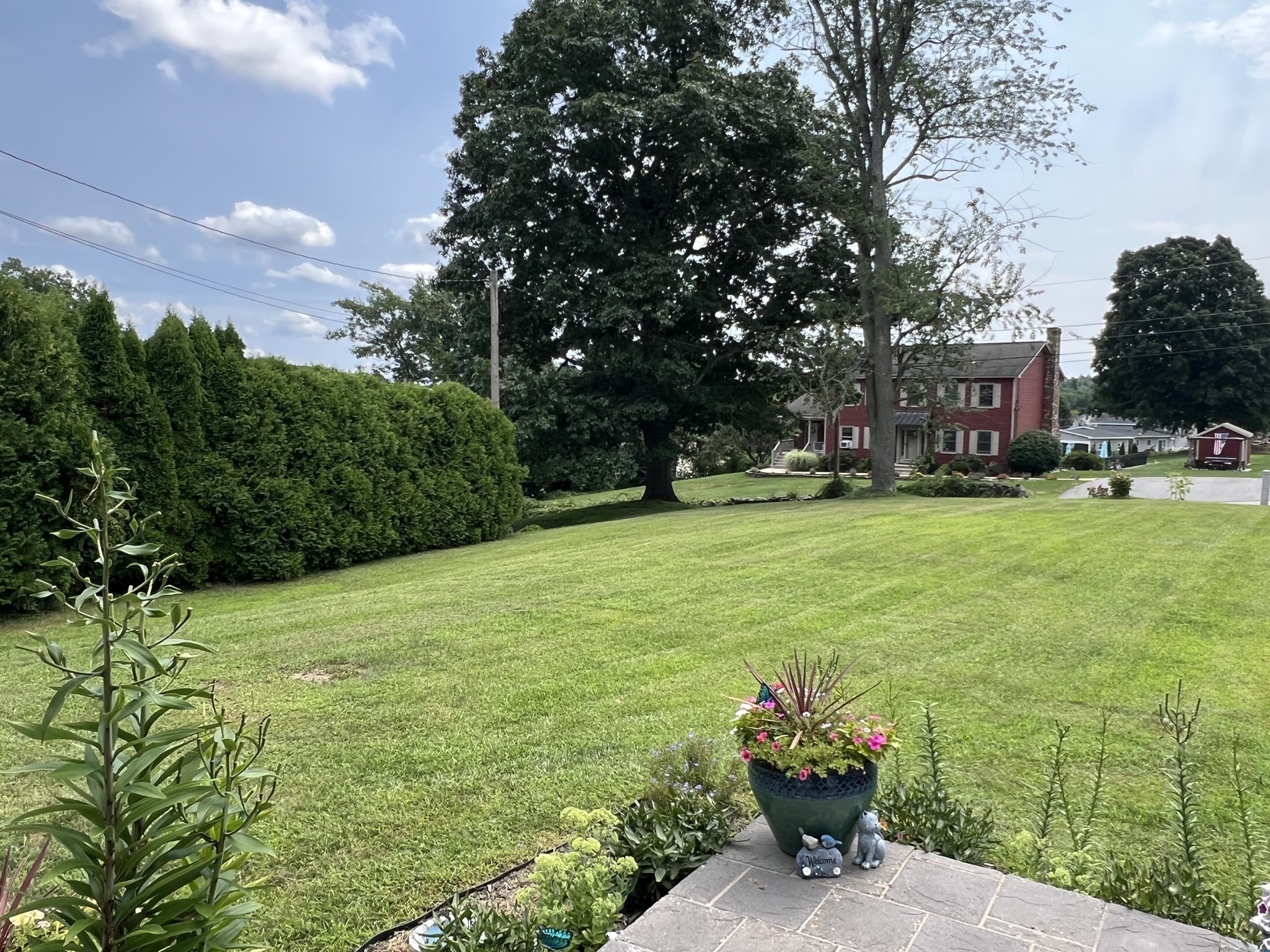 Sloping lawn and flower-bordered patio facing a red house beneath mature trees.