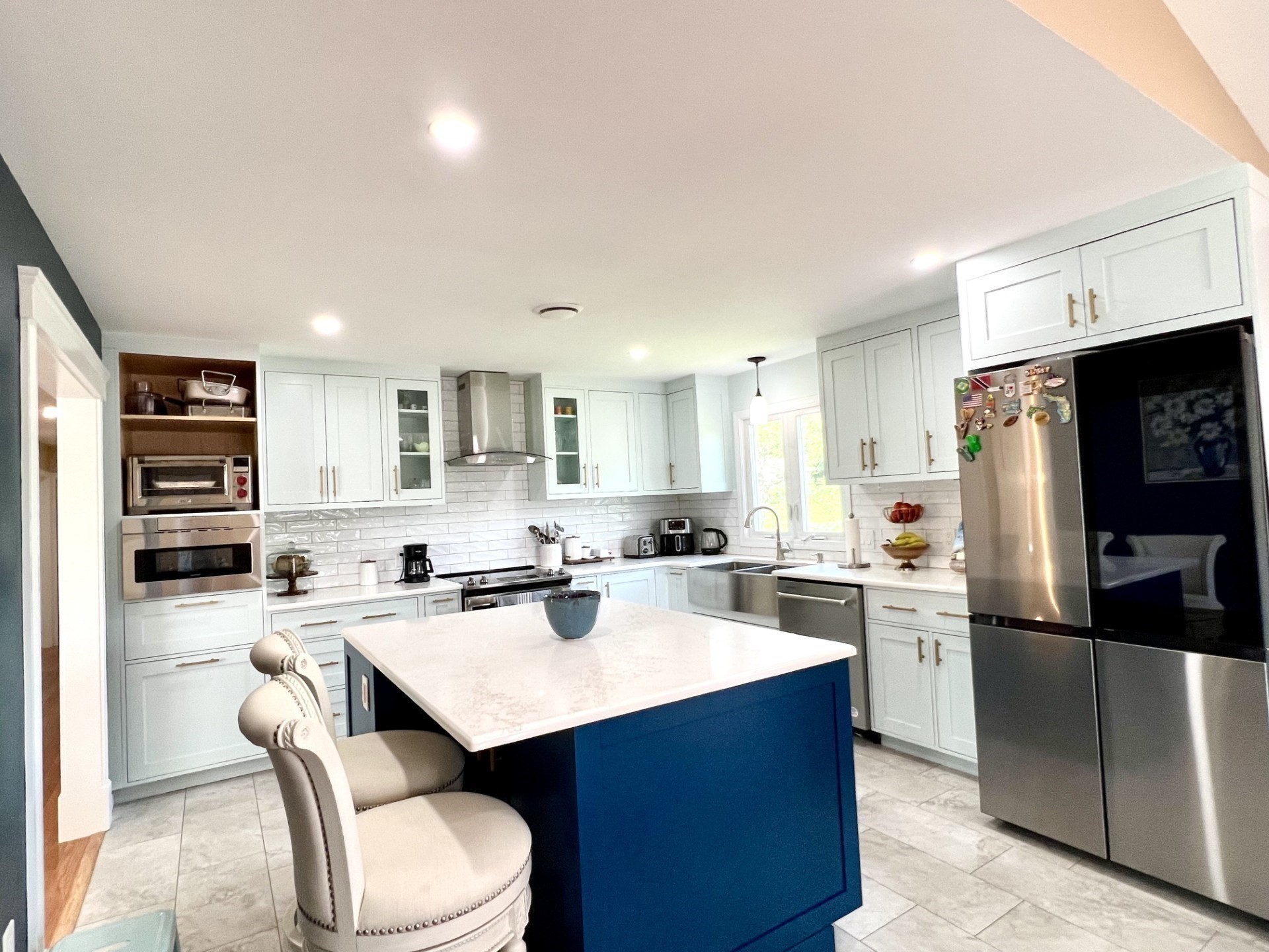 Bright kitchen with a blue island, white cabinetry, stainless appliances, and a tiled backsplash.