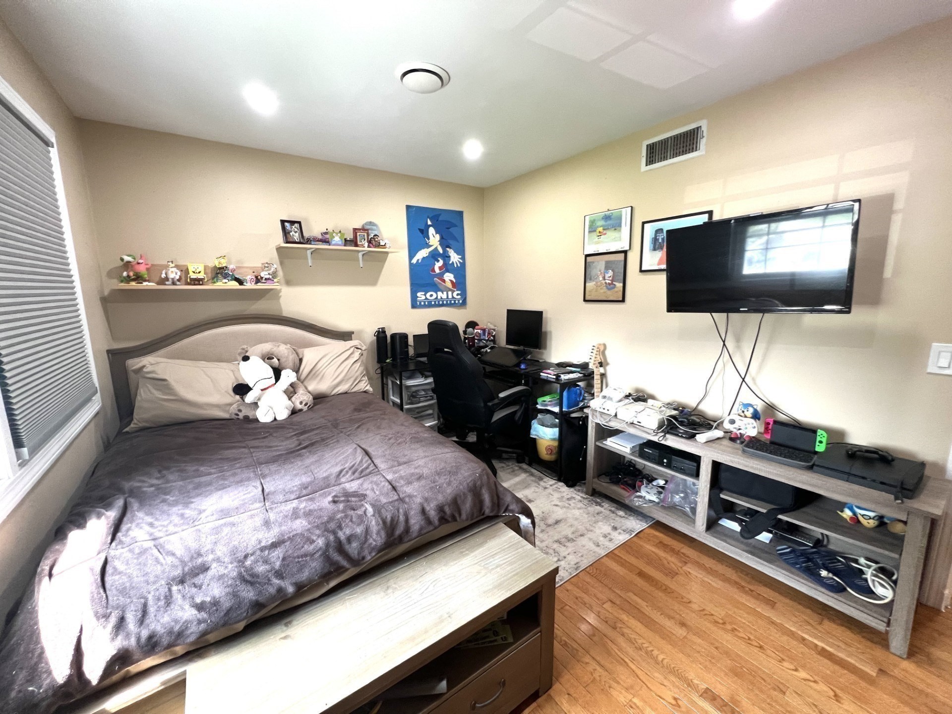 Bedroom with a bed, plush toys, gaming desk, and wall-mounted television.
