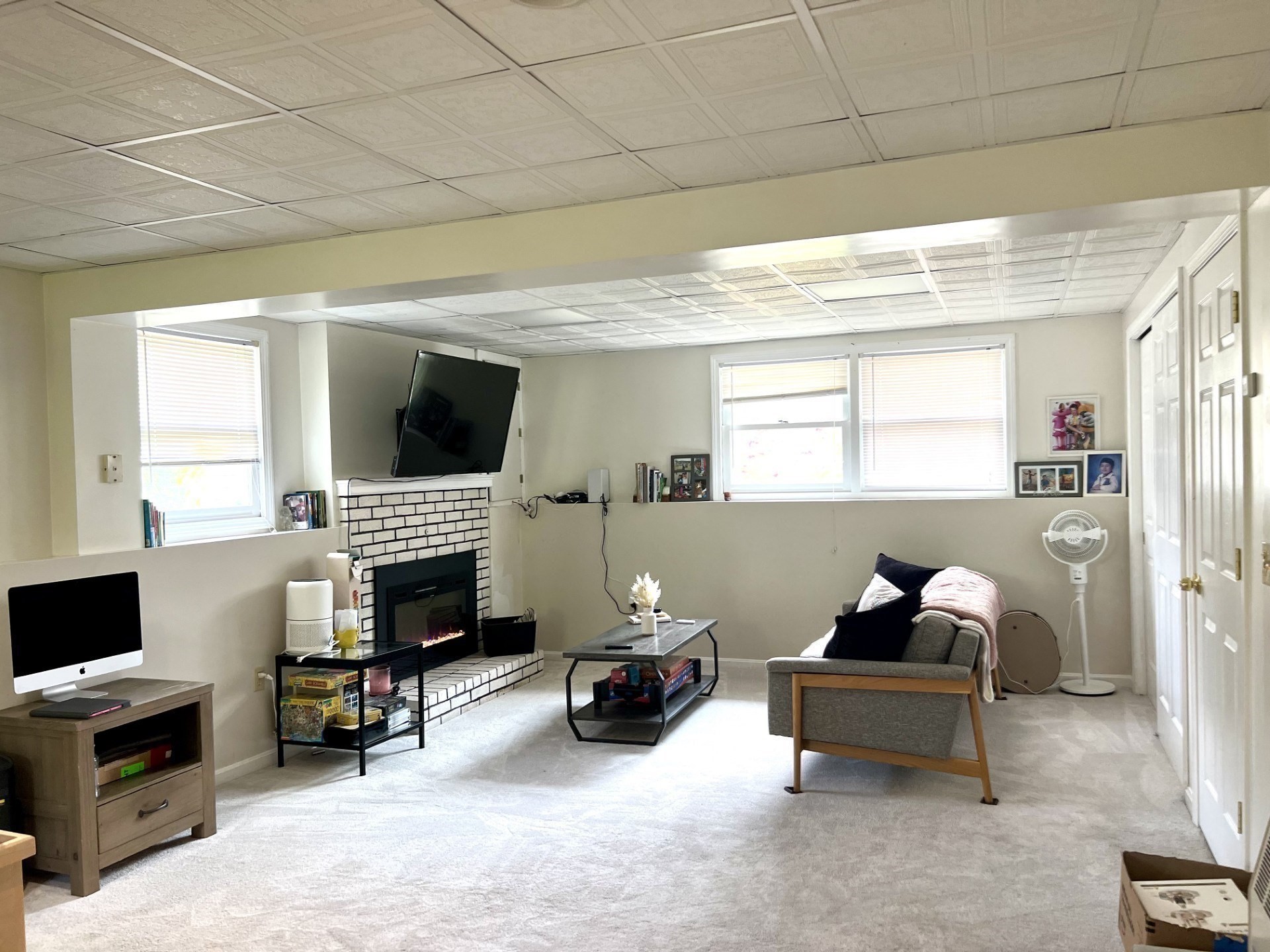 Living room with a white brick fireplace, mounted television, gray sofa, and light carpet.