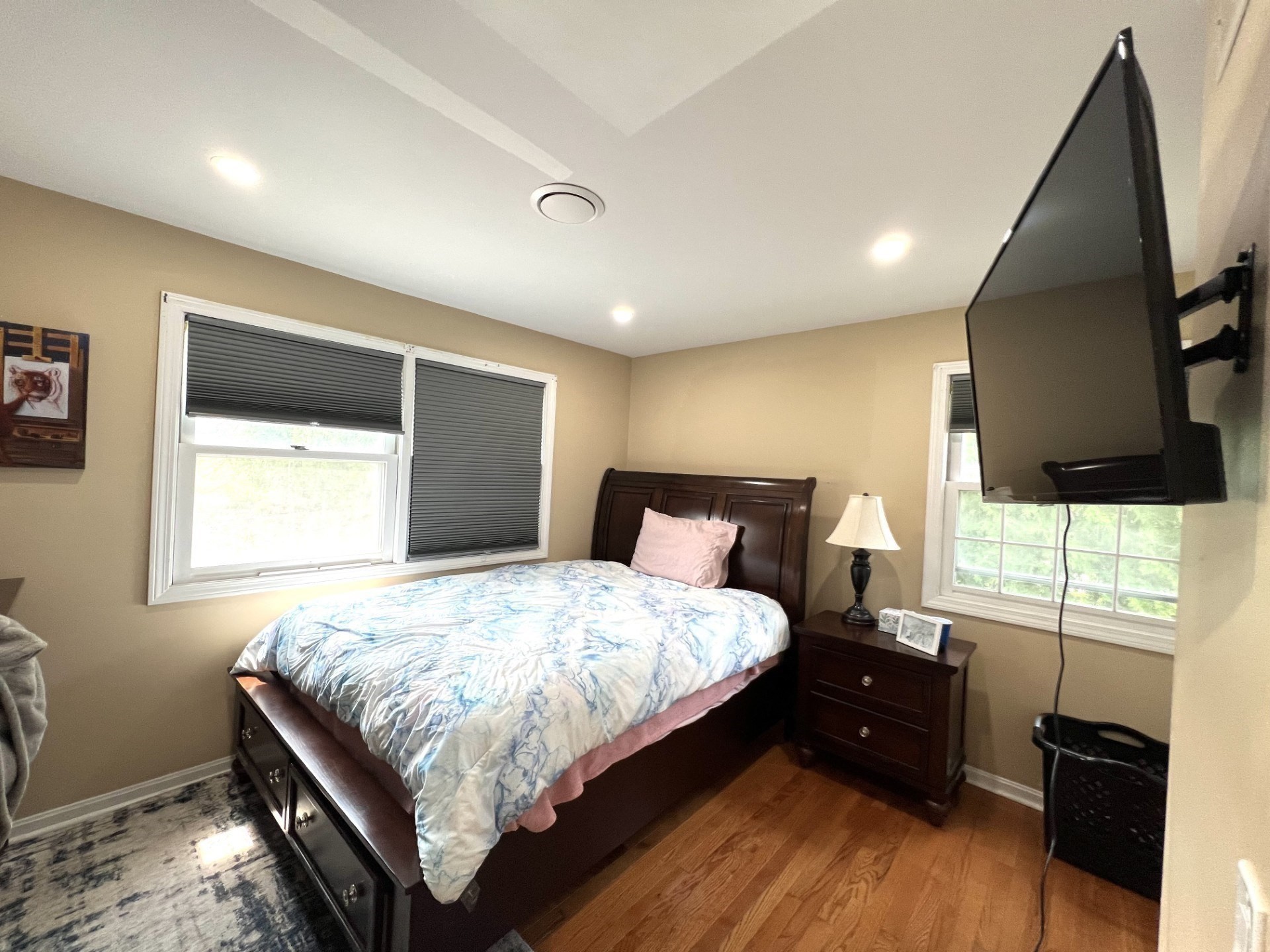 Bedroom with a dark wood bed, blue-and-white bedding, hardwood floors, and a wall-mounted television.