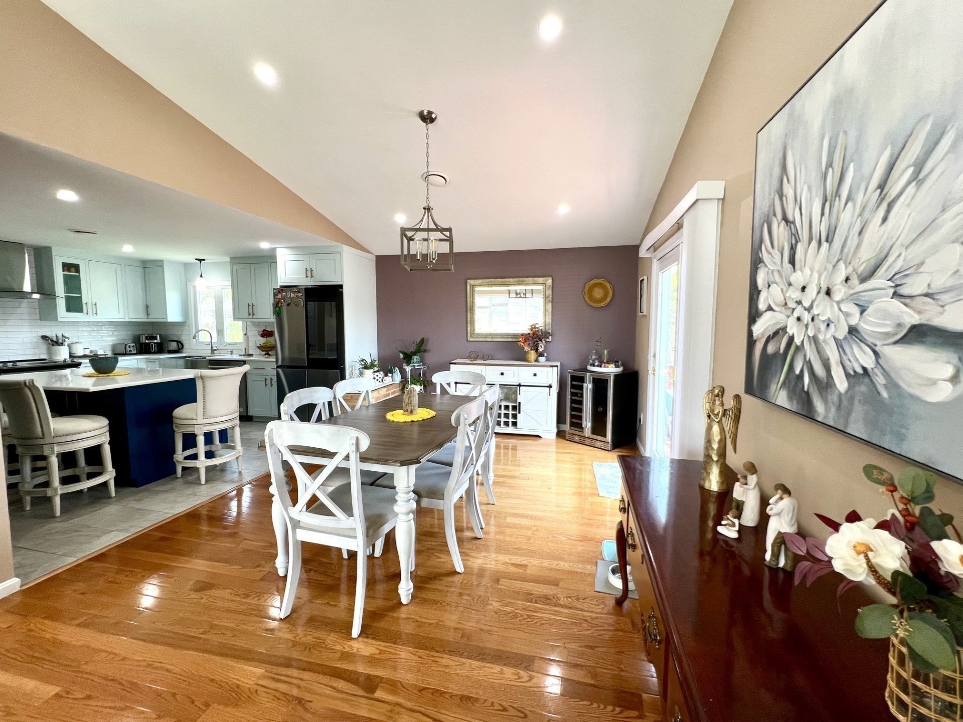 Open dining room and kitchen with hardwood floors, white cabinetry, and a dark wood table with white chairs.