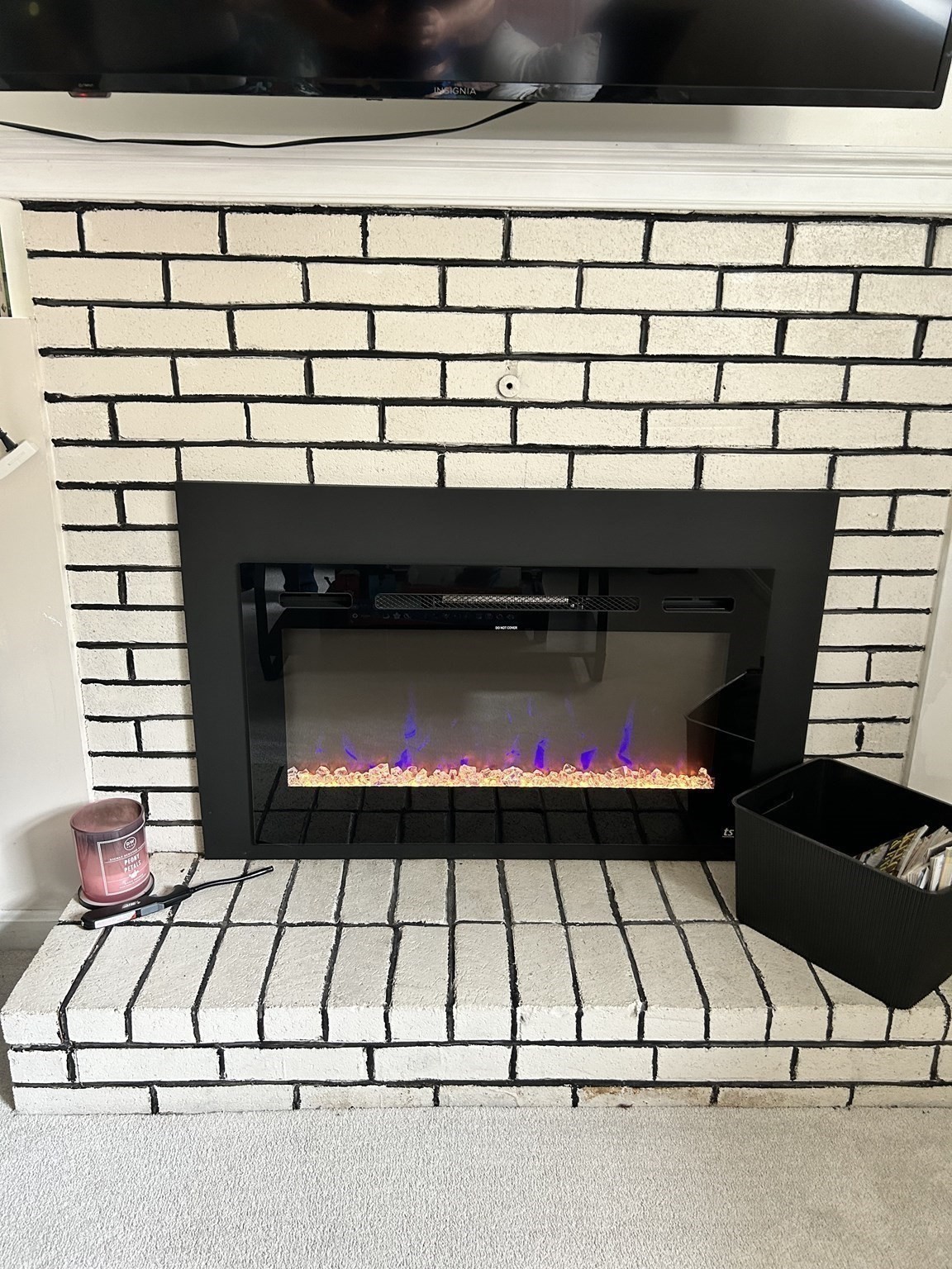 Black electric fireplace with purple and orange flames in a white brick surround and raised hearth.