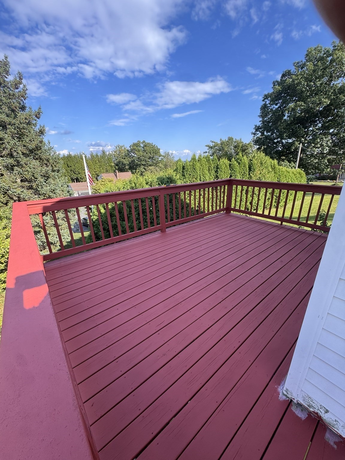 Red wooden deck with matching railings overlooking leafy trees and hedges.