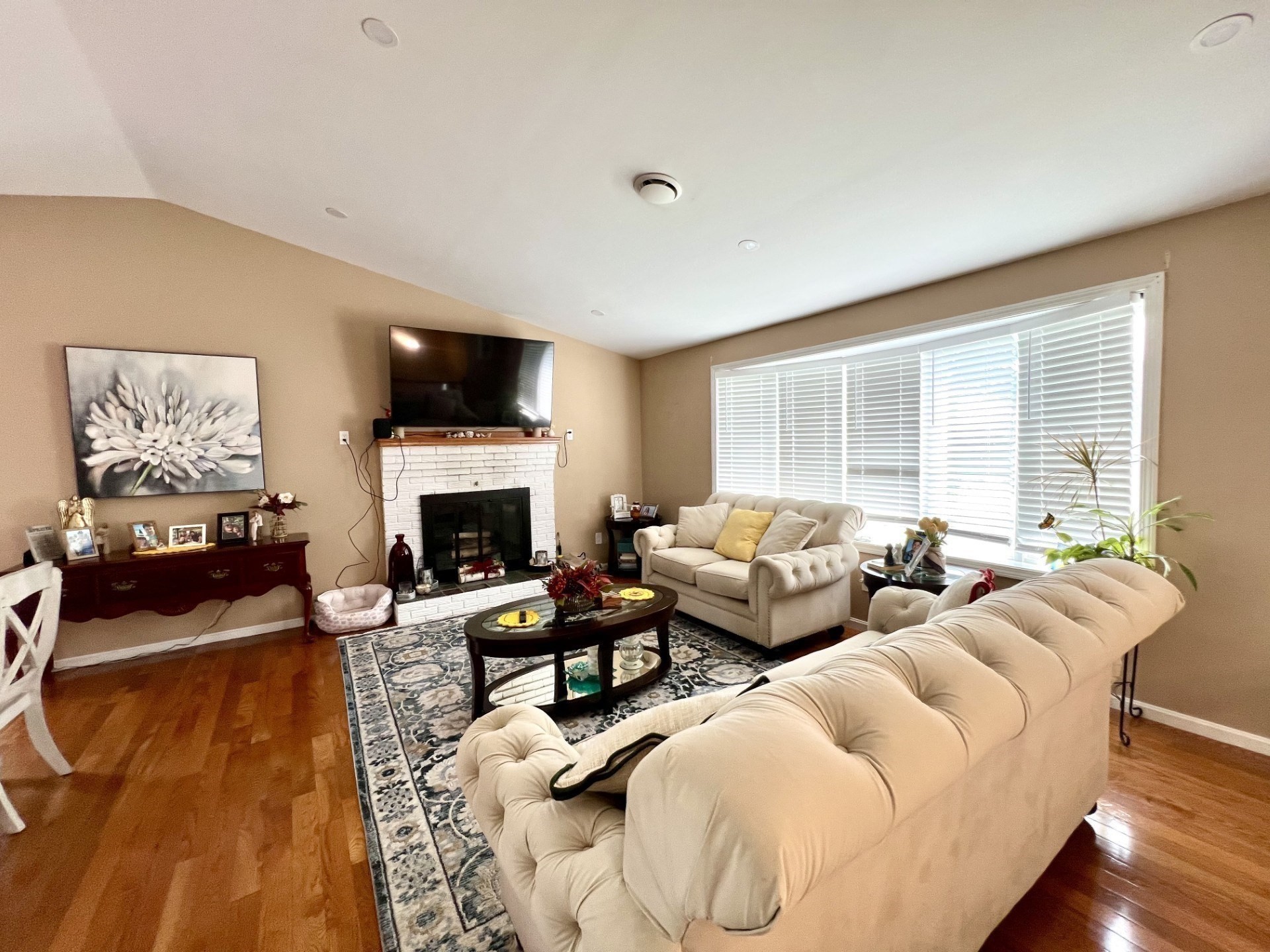 Furnished living room with a white brick fireplace, cream sofas, and large windows.