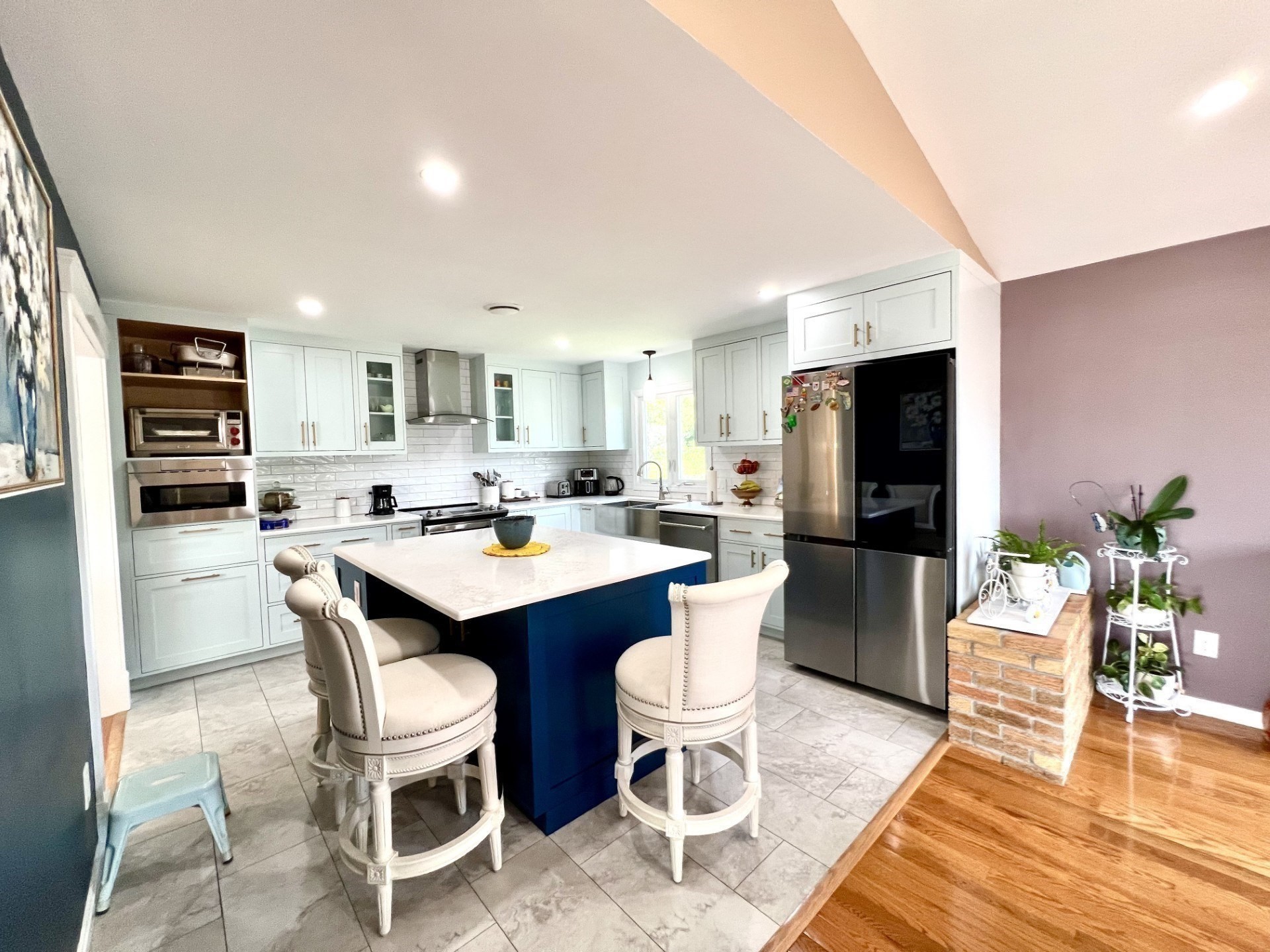 Kitchen with pale blue cabinets, stainless steel appliances, and a deep blue island with white bar stools.