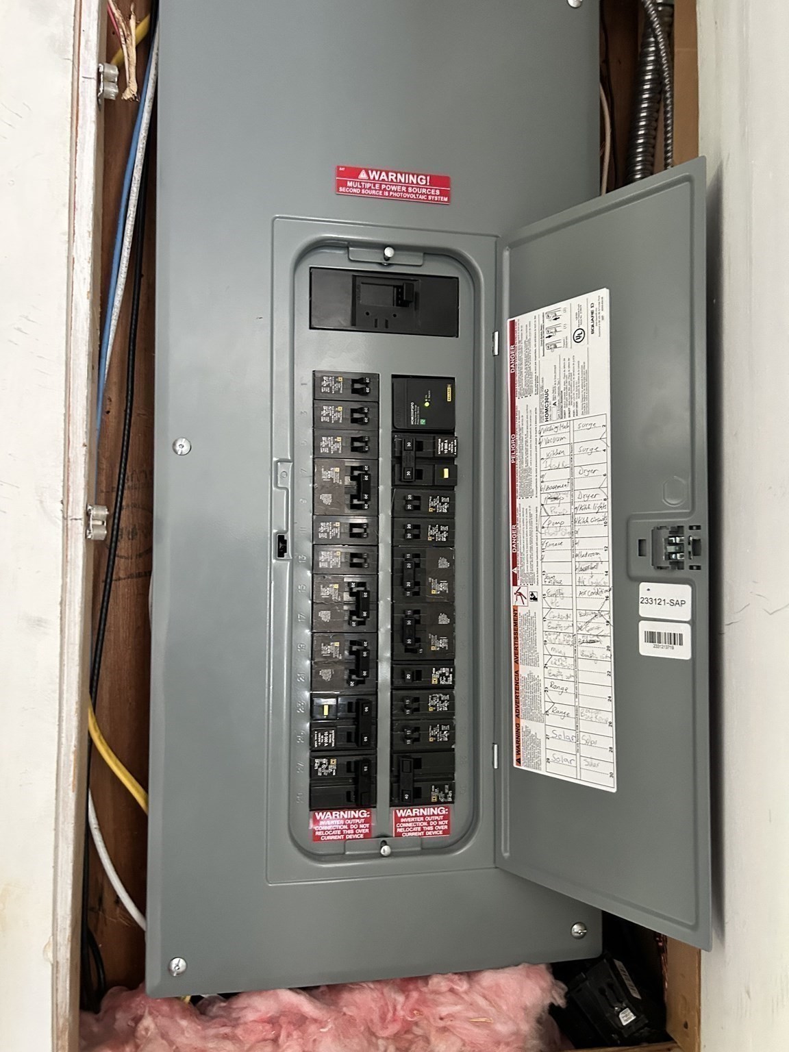 Open electrical breaker panel with rows of circuit breakers and a handwritten directory on its door.
