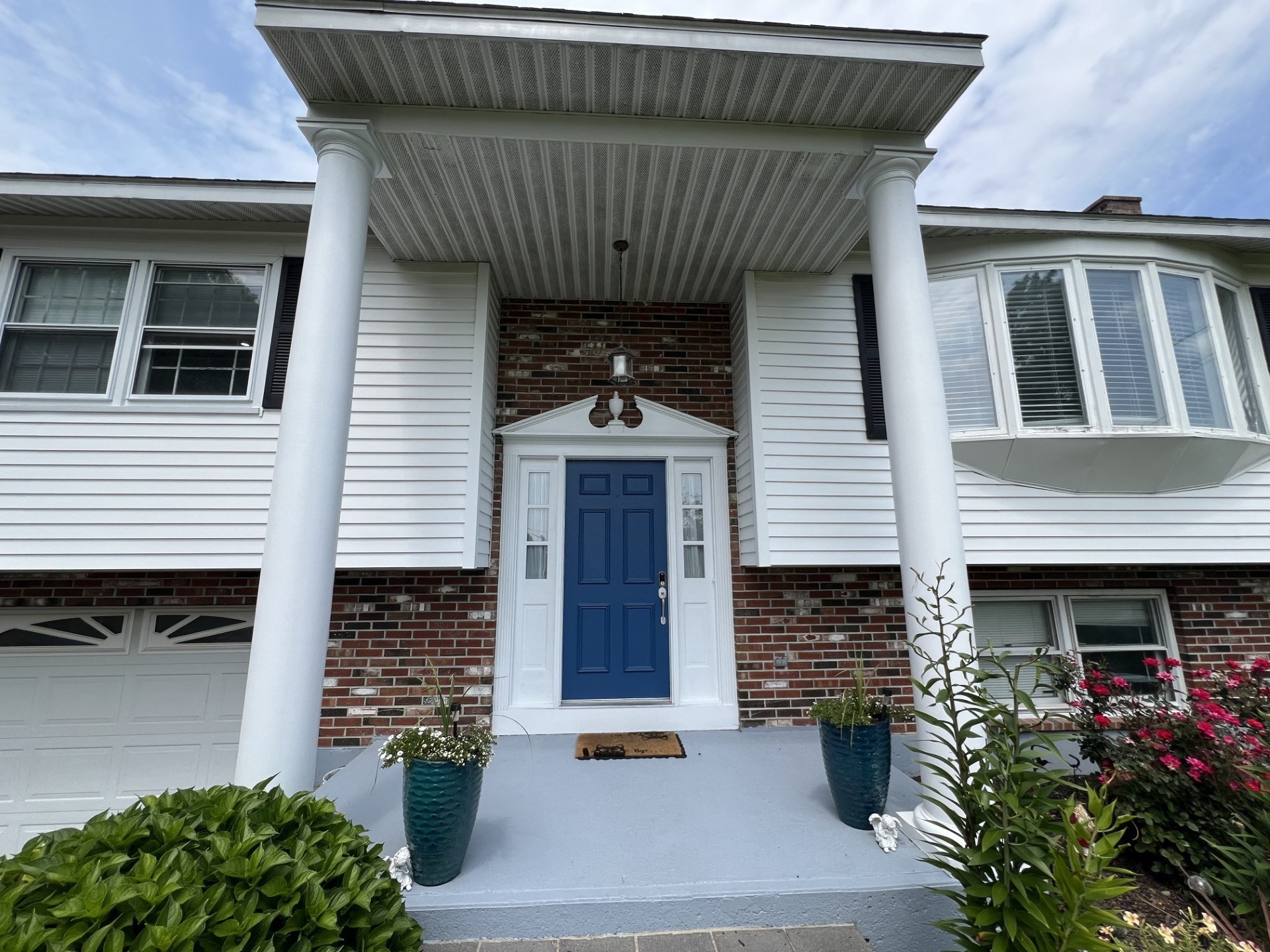 House entrance with a blue door, brick facade, and covered porch with white columns.
