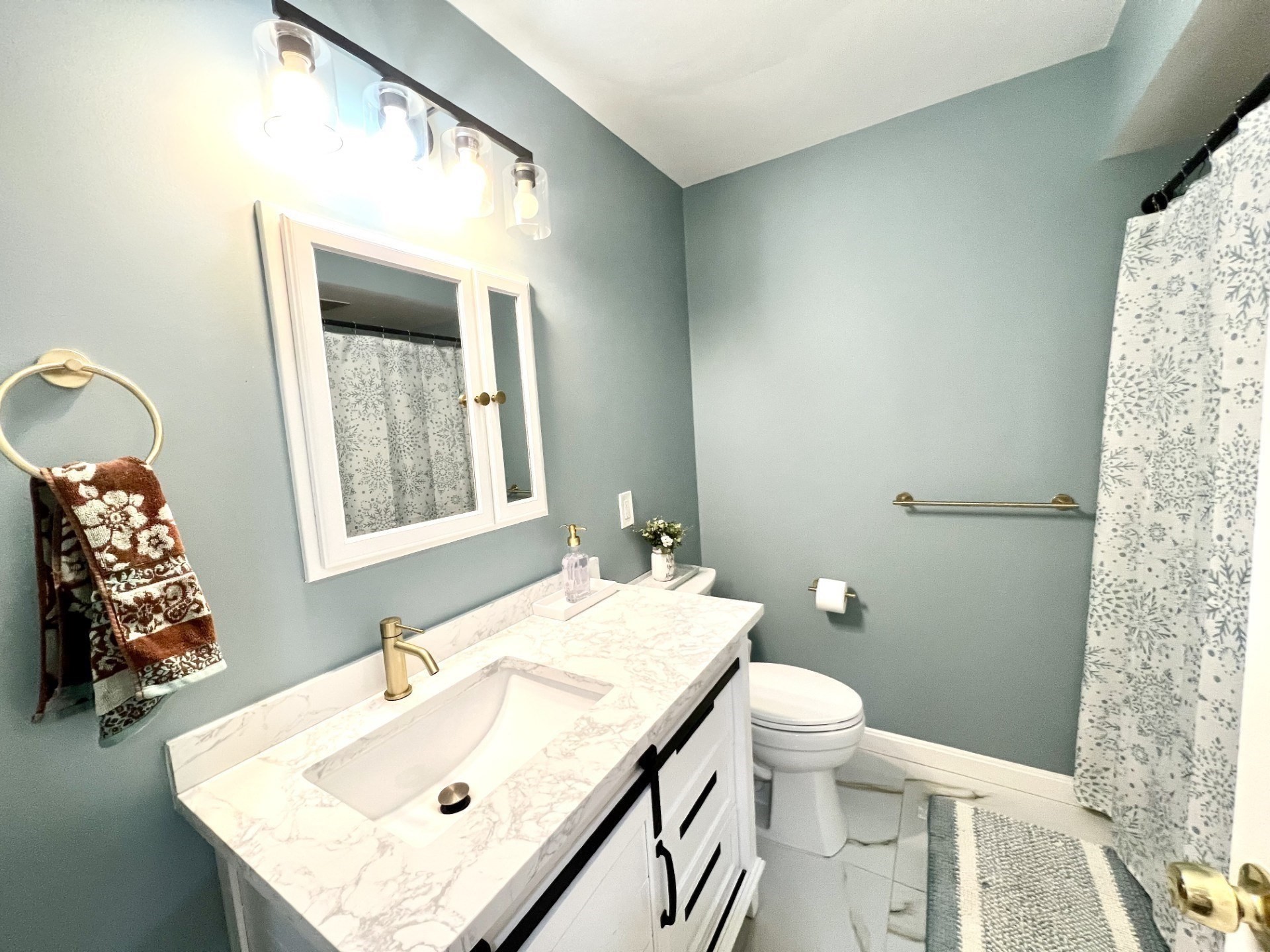 Bathroom with a marble-topped white vanity, gold fixtures, and a patterned shower curtain.