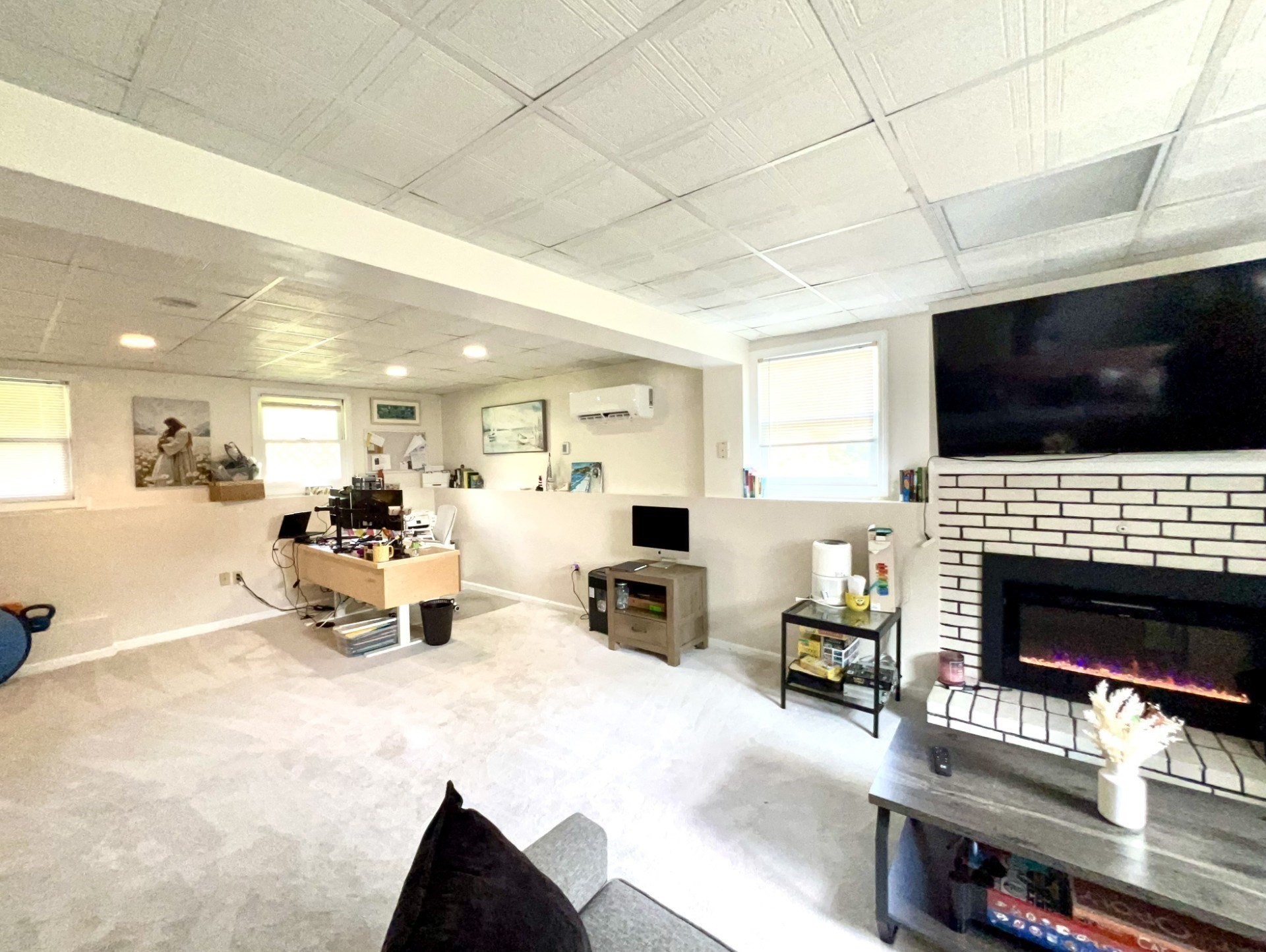 Furnished living room with a white brick fireplace, wall-mounted television, and desk area.