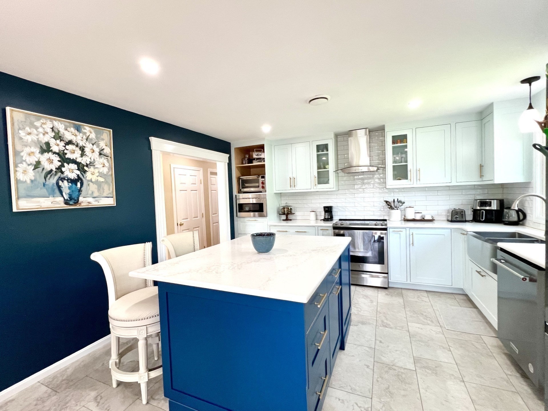 Kitchen with a large blue island, white cabinets, stainless steel appliances, and a navy accent wall.
