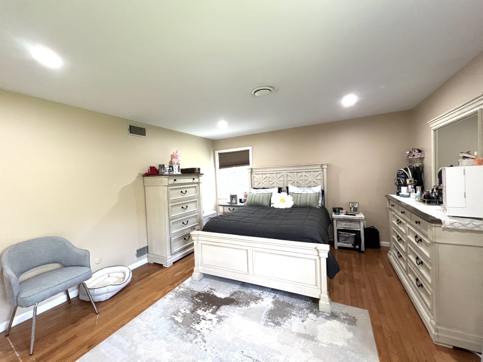 Furnished bedroom with a white bed, dark bedding, hardwood floors, and a gray chair.