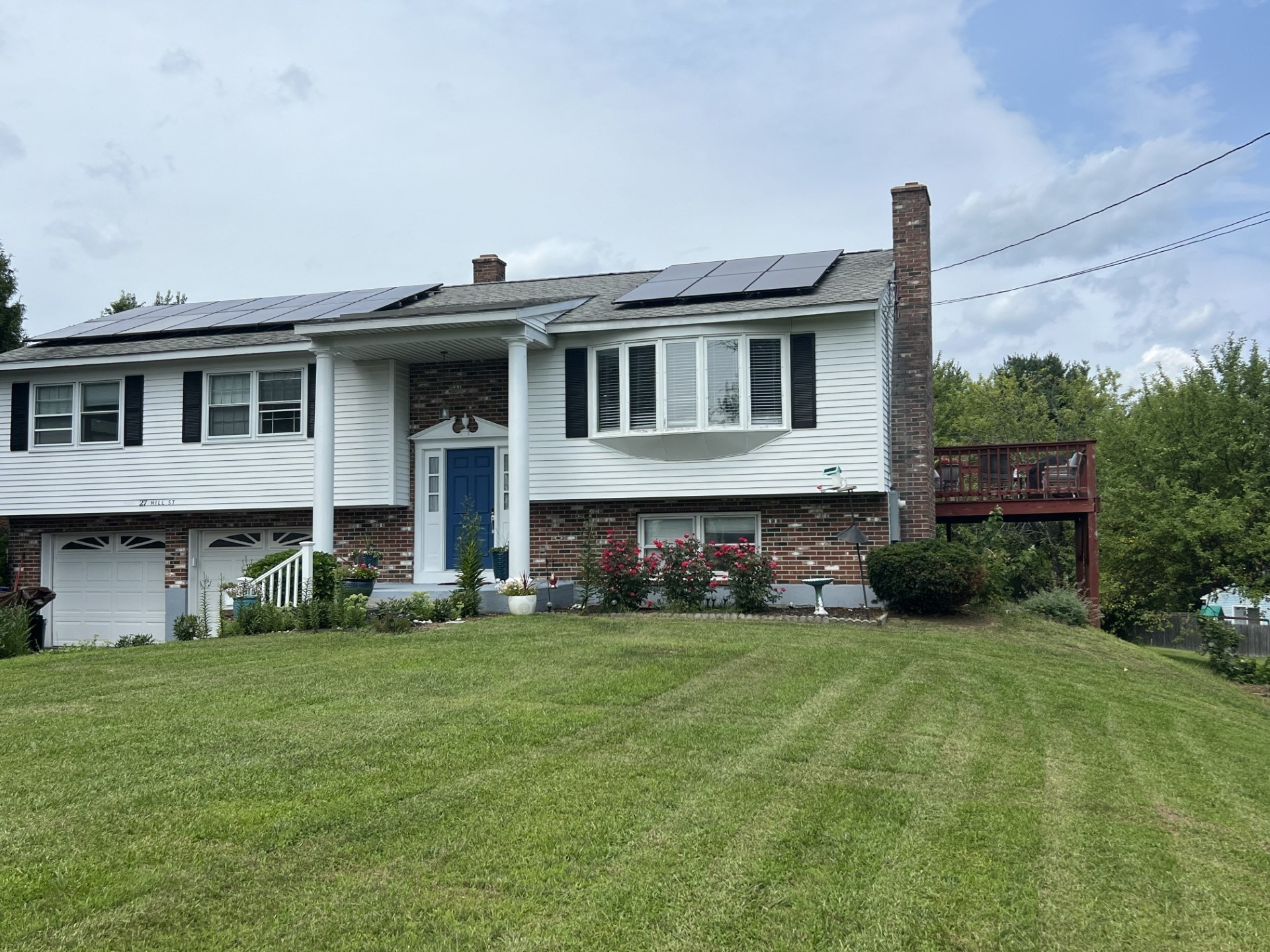 Split-level home with rooftop solar panels, a blue front door, attached garage, and raised deck.