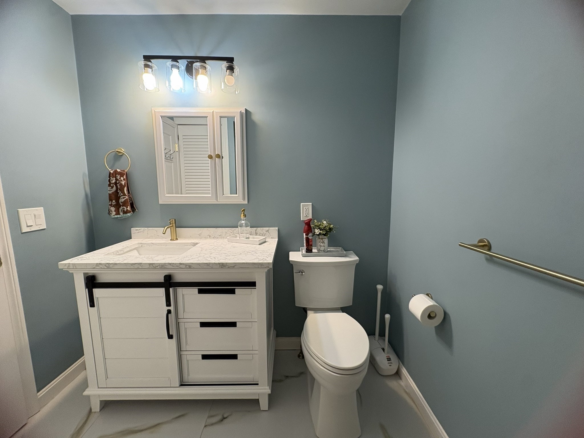 Bathroom with a white vanity, marble-look counter, toilet, and blue-gray walls.