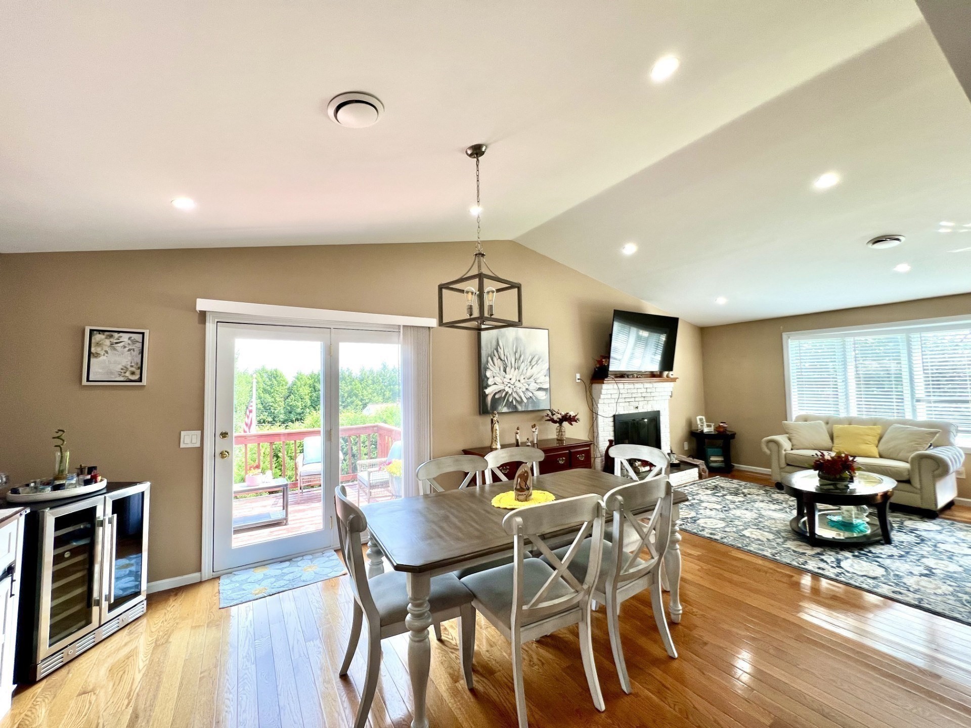 Open-plan dining and living room with hardwood floors, a white brick fireplace, and sliding doors to a deck.