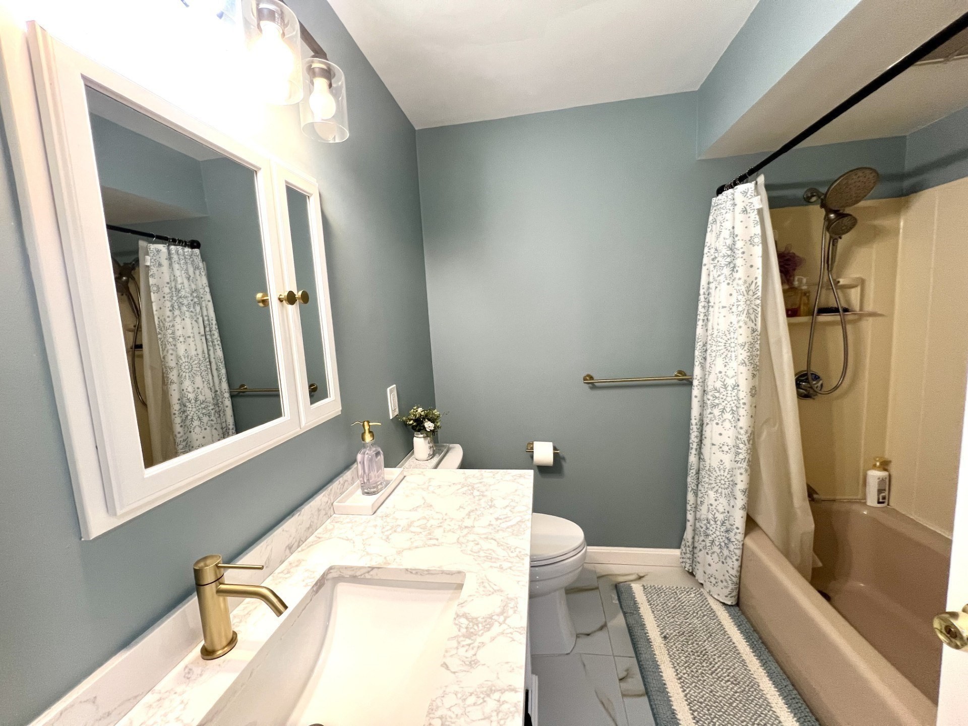 Bathroom with a marble-look vanity, brass fixtures, blue-gray walls, and a patterned shower curtain.