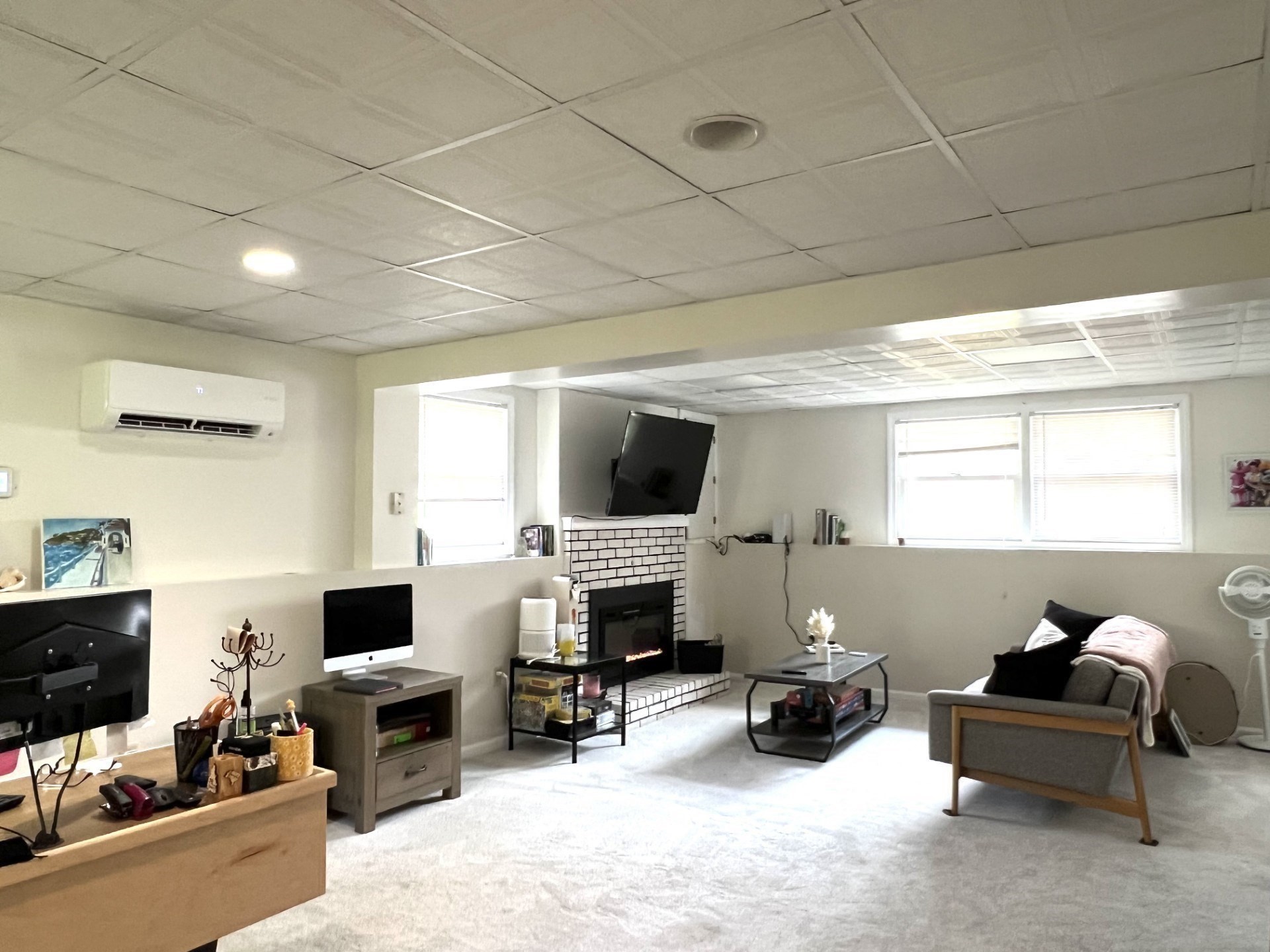 Furnished lower-level living room with white brick fireplace, mounted television, and carpeted floor.