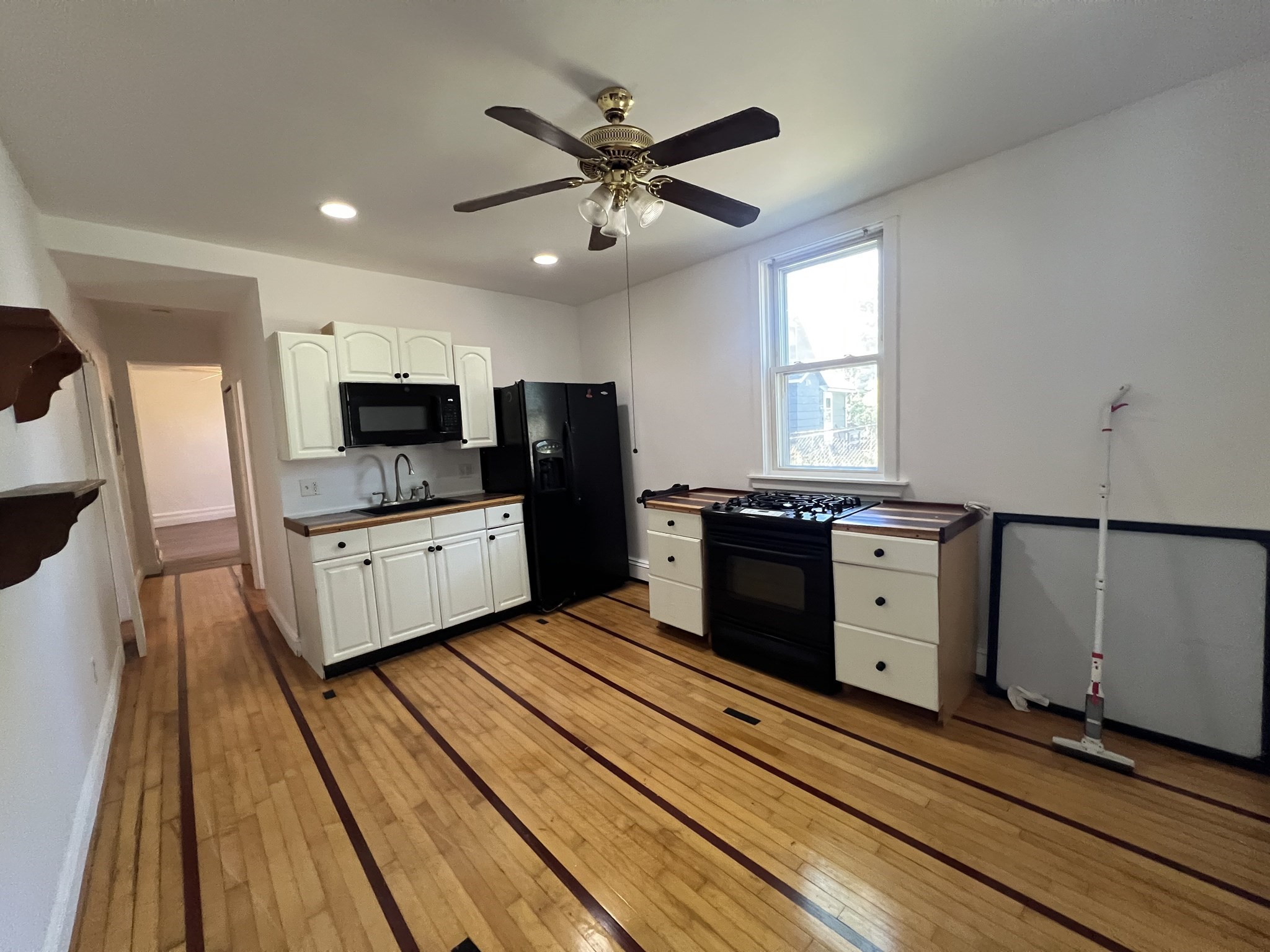 Kitchen with white cabinets, black appliances, and hardwood flooring with dark inlay strips.