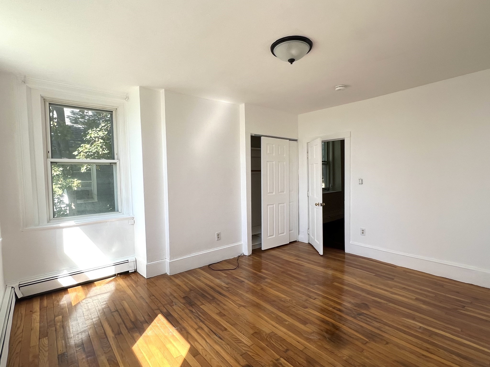Vacant bedroom with hardwood floors, a large window, and open closet doors.