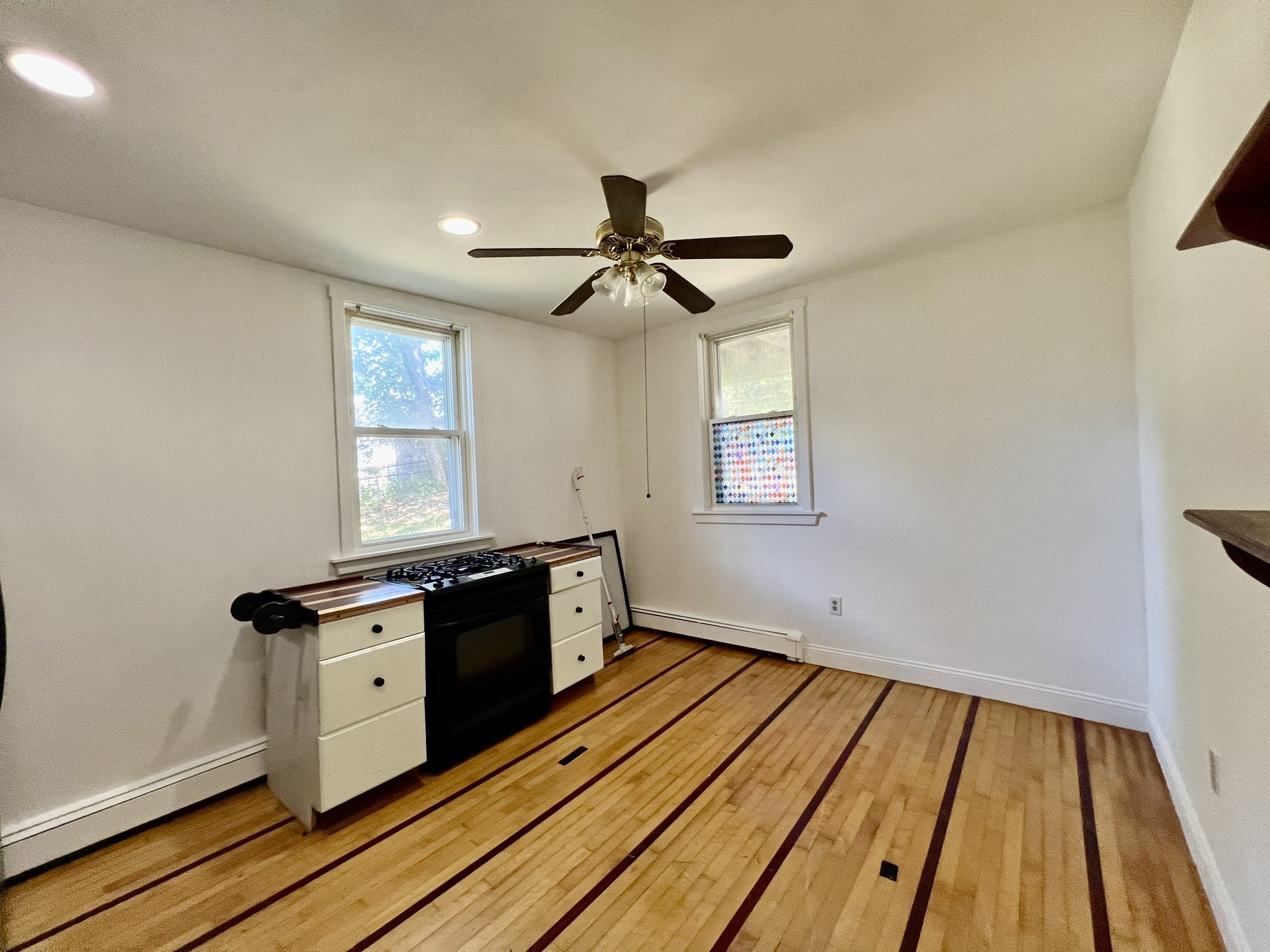 Mostly empty kitchen with a black gas range, ceiling fan, and striped hardwood floor.