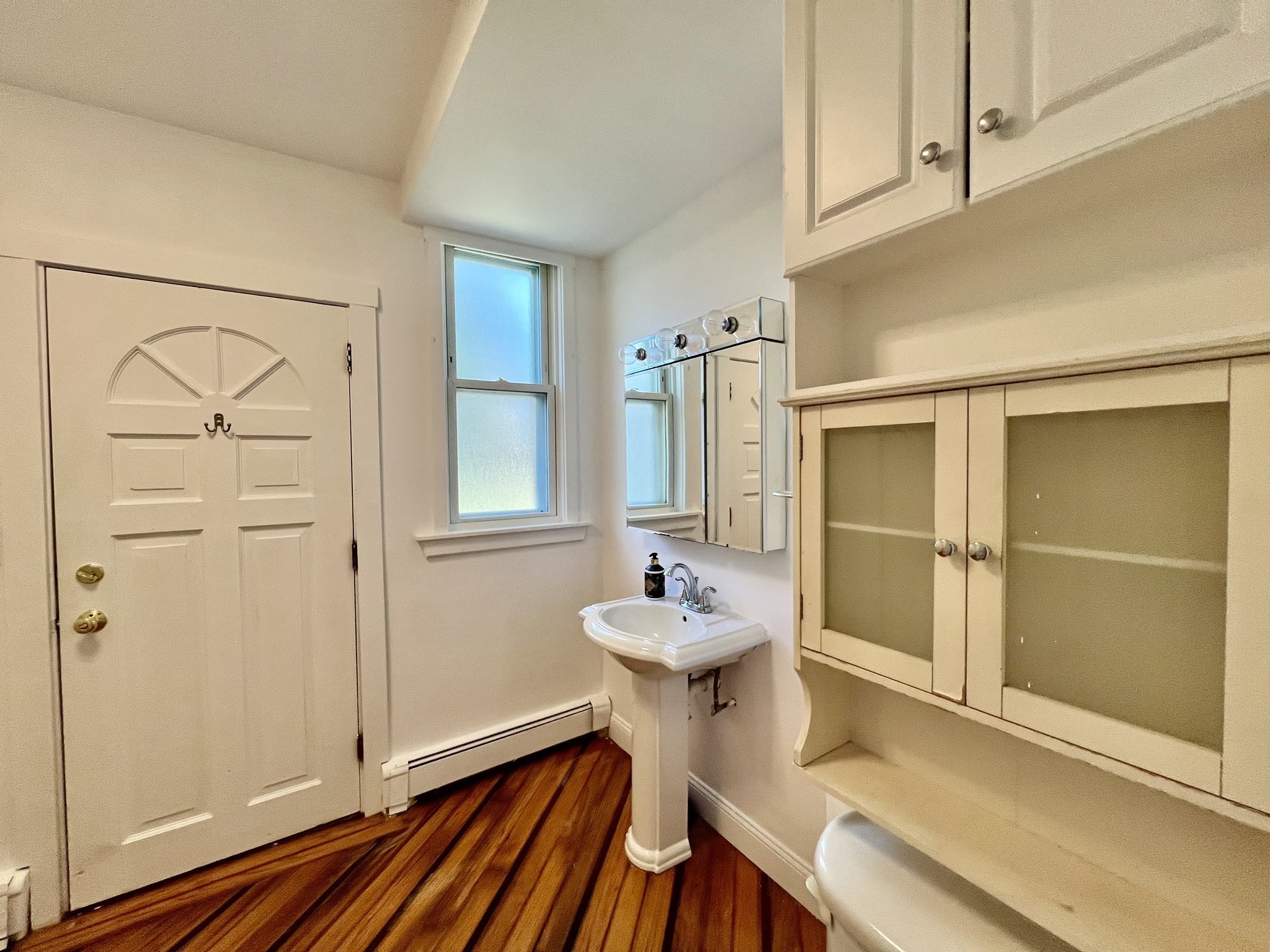 Small washroom with a pedestal sink, mirrored medicine cabinet, built-in cabinets, and hardwood flooring.
