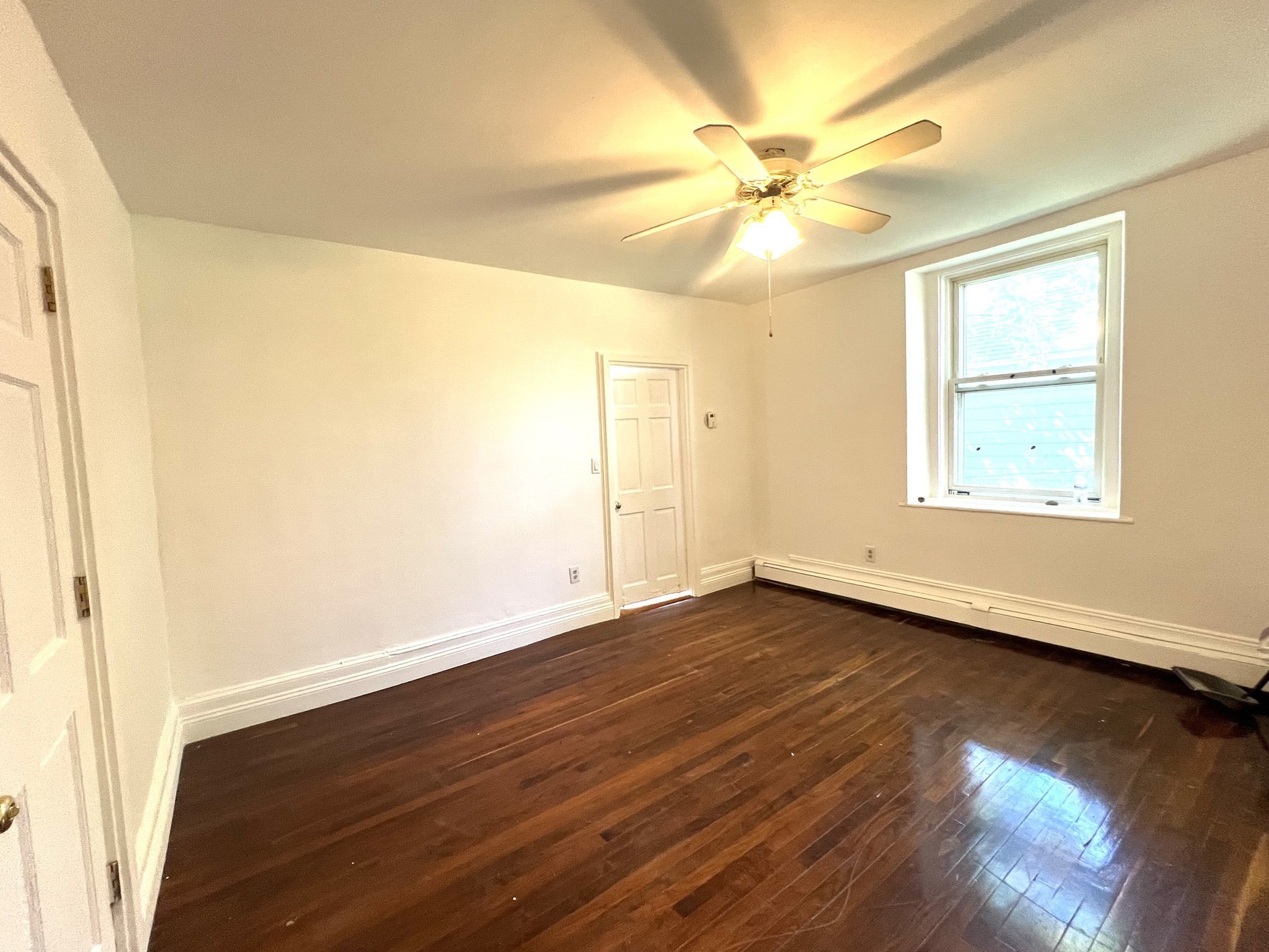 Vacant room with dark hardwood floors, a ceiling fan, and a single window.