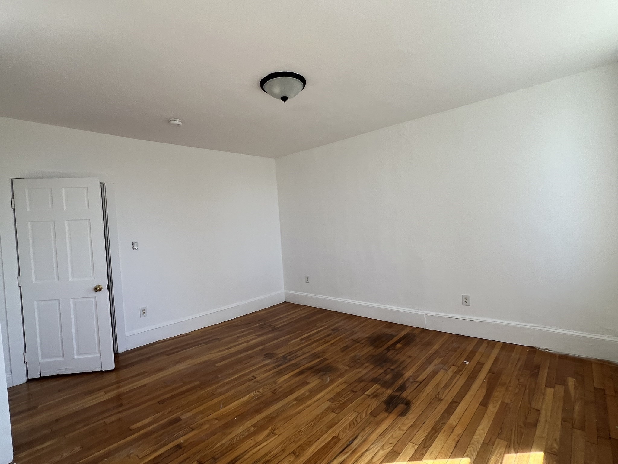 Empty room with hardwood floors, white walls, and a ceiling light.