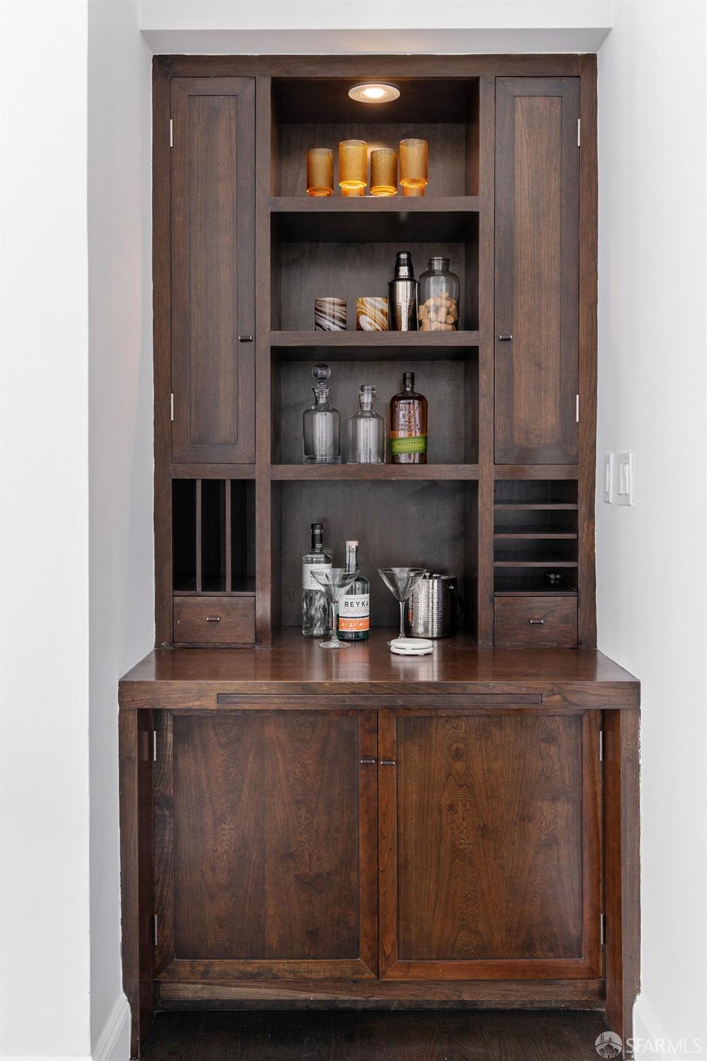 Built-in dark wood bar cabinet with illuminated display shelves and cocktail accessories on the counter.