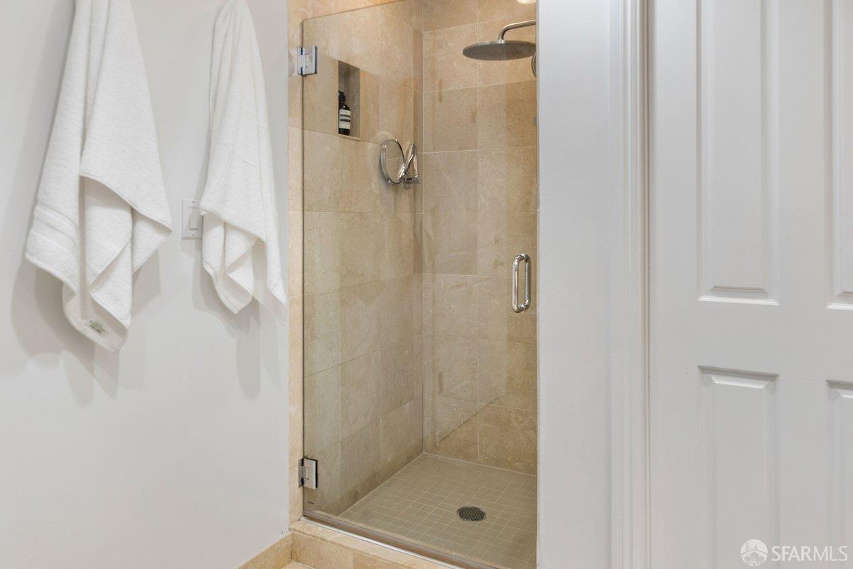 Bathroom shower with beige stone tile, glass enclosure, and white towels.